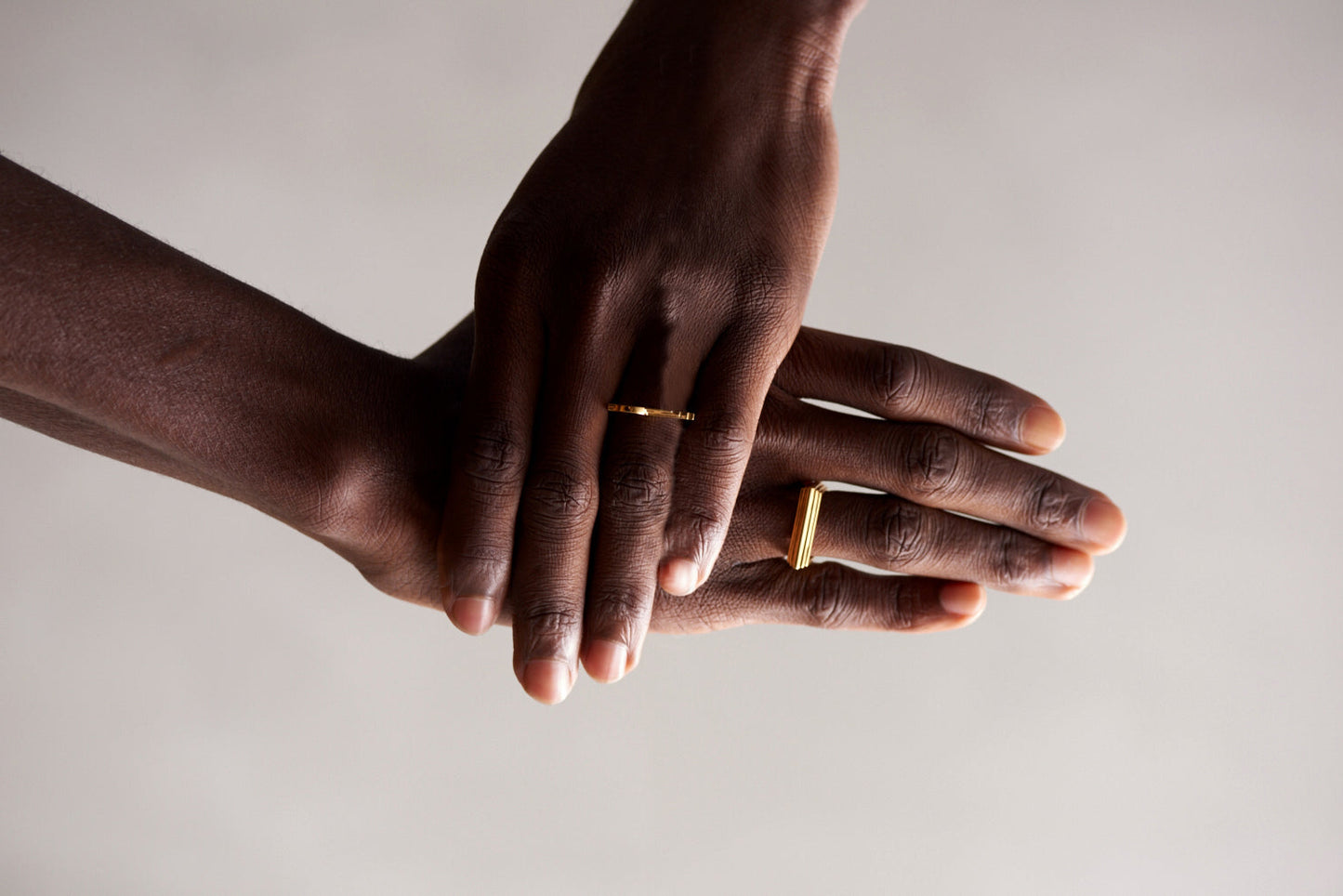 Two hands with gold rings on a neutral background