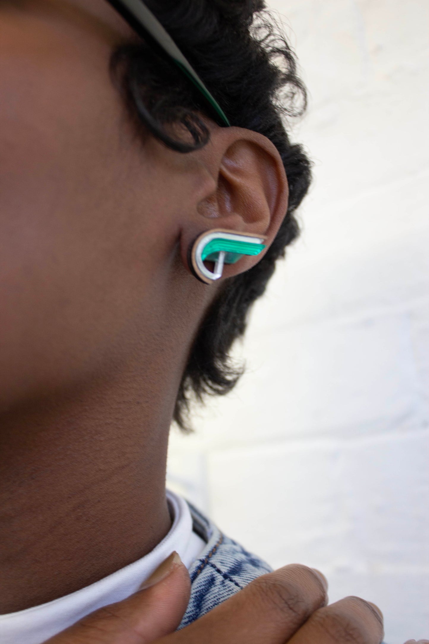 Close-up of an ear wearing a green and silver earring resembling a semi heart shape against a white background. Laser cut earring made from plywood, walnut wood and acrylic