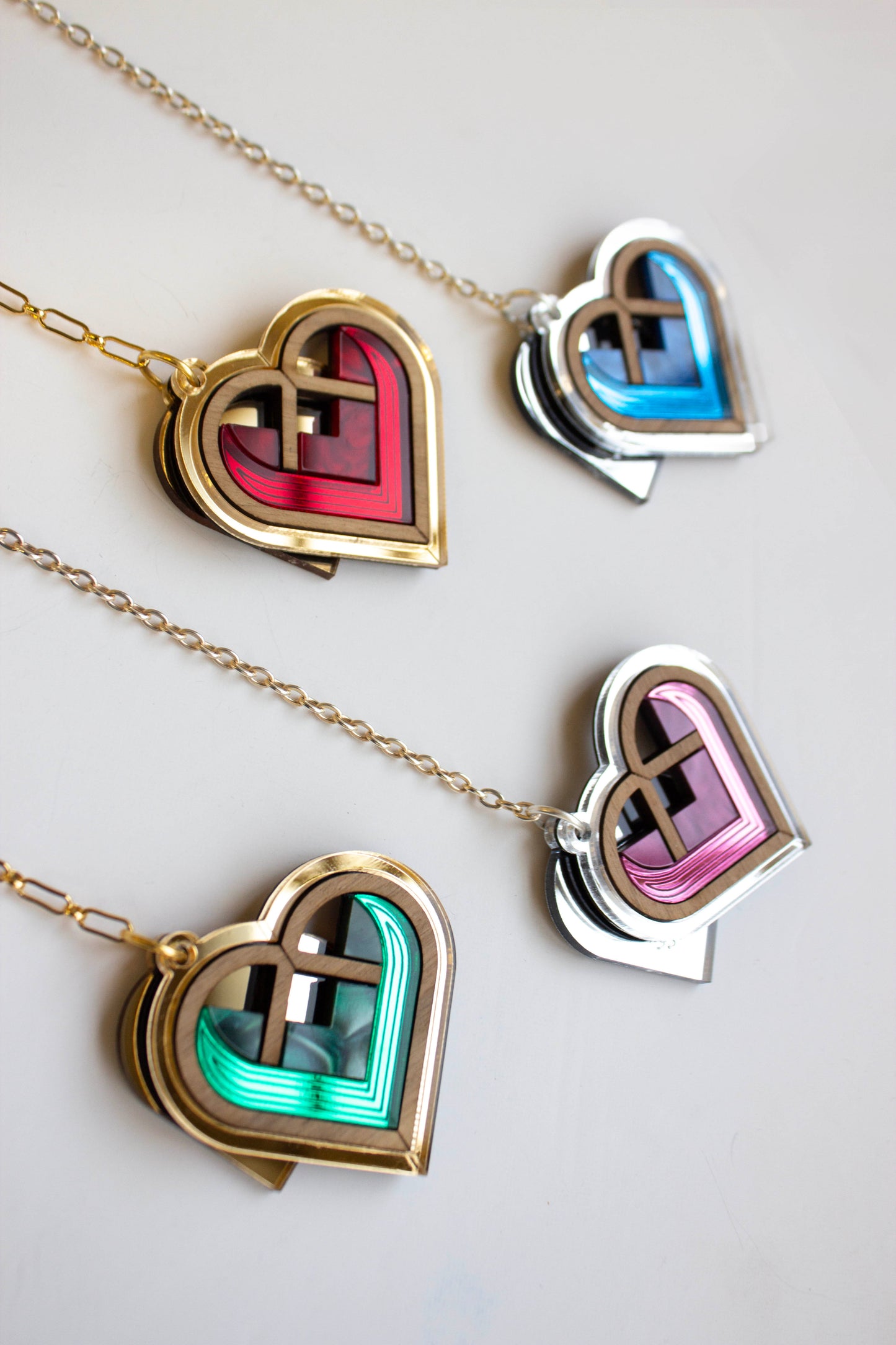 Heart-shaped bag charm with colorful interior designs and gold/ silver chains on a white background. Laser cut bag charms made from plywood, walnut wood and acrylic