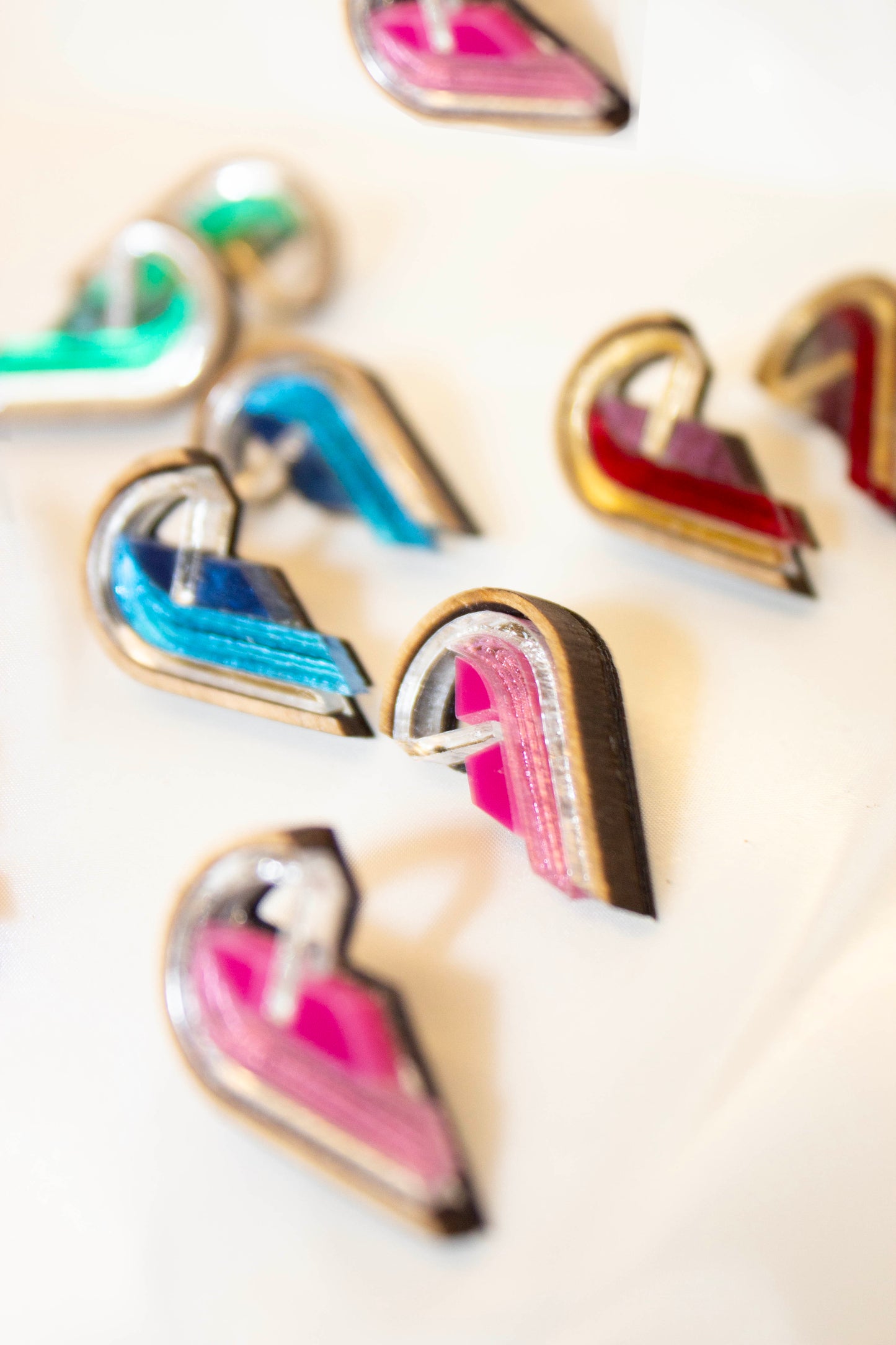 Colorful semi heart-shaped earrings on a white surface. Made from plywood, acrylic and walnut wood