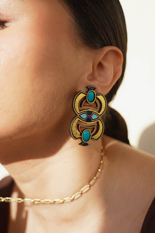 Close-up of a person wearing a decorative scarab earring with turquoise stones and gold accents.
