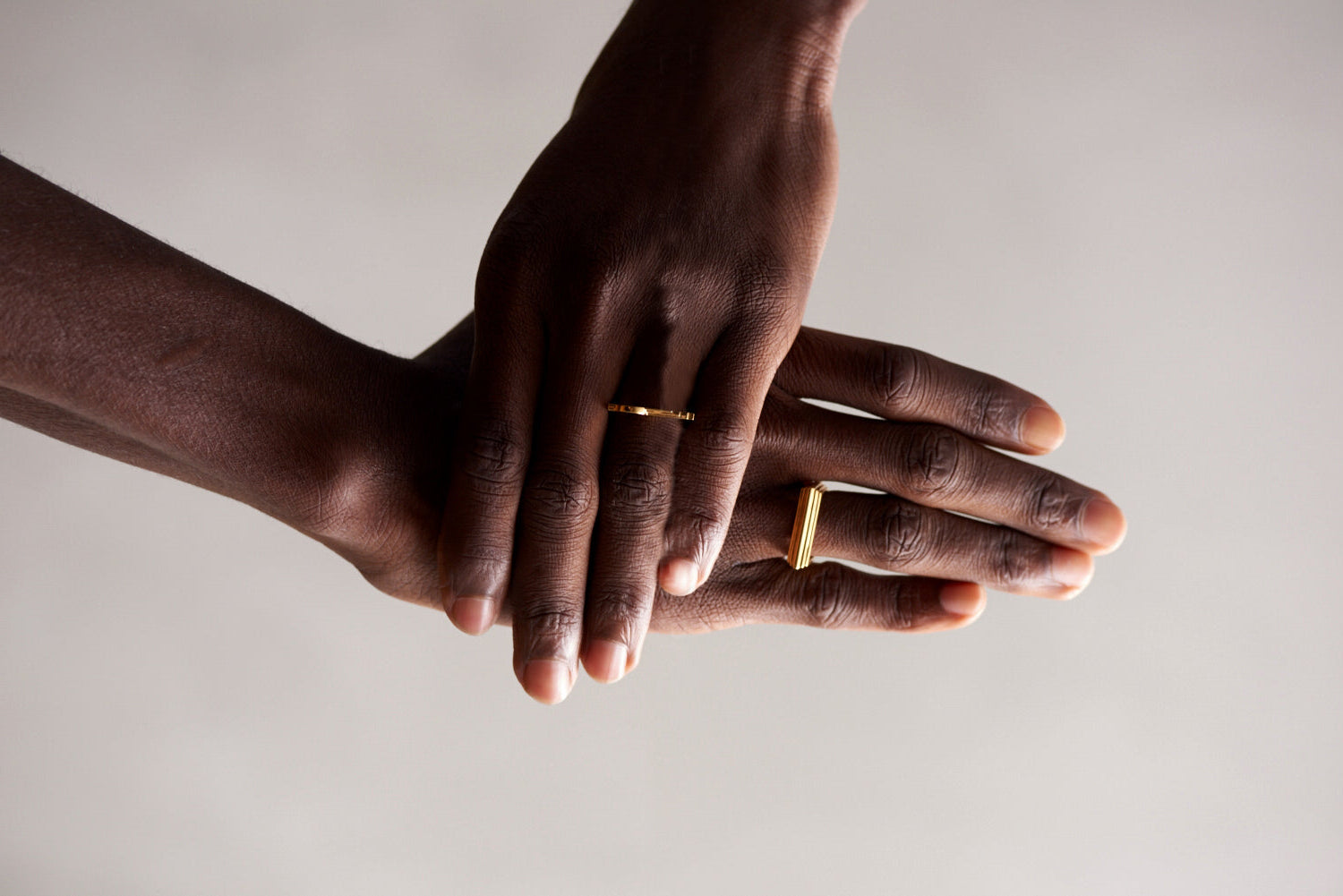 Two hands with gold rings on a neutral background