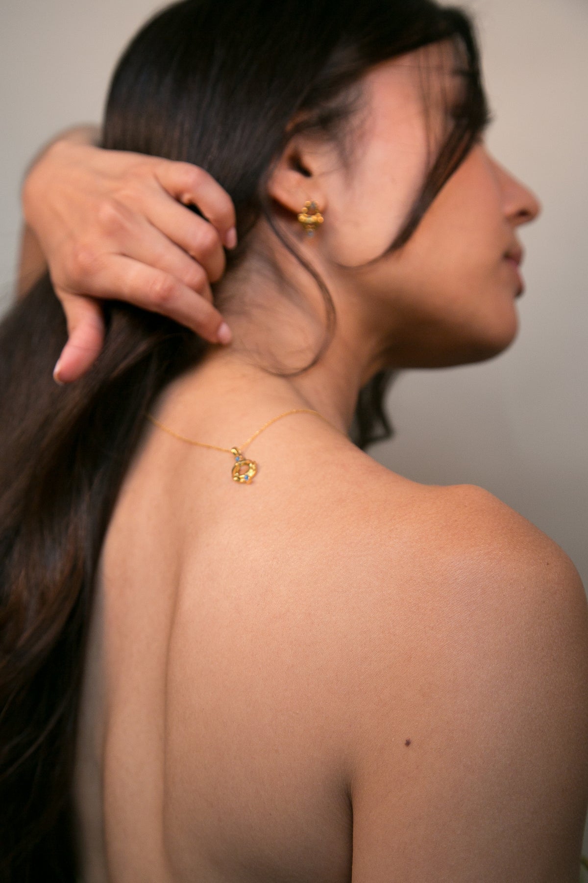 Woman with a gold and blue topaz gemstone necklace and earrings. Her hand adjusting her hair against a neutral background