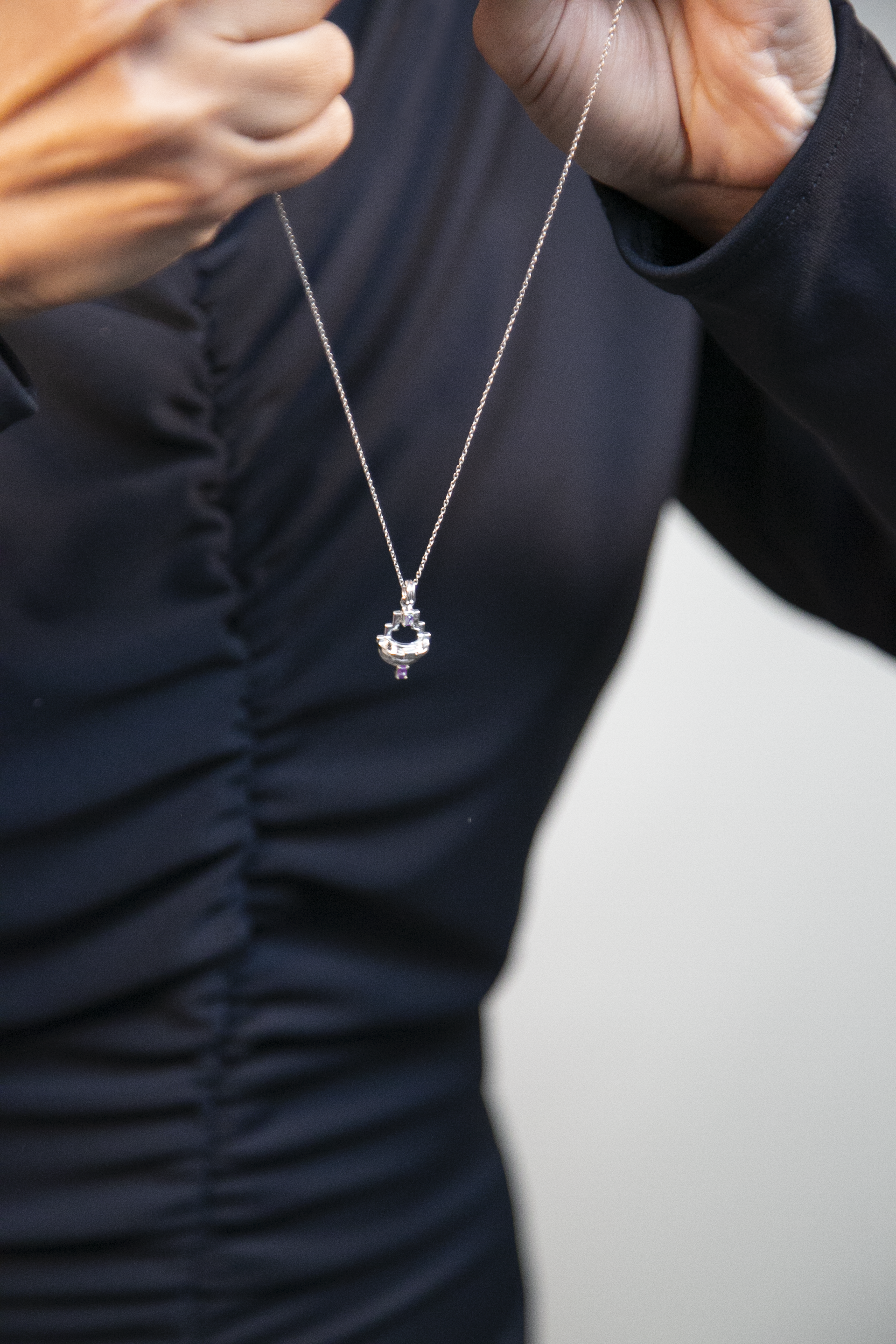 close up of a woman wearing a silver geometric necklace with purple amethyst gemstones against a grey background