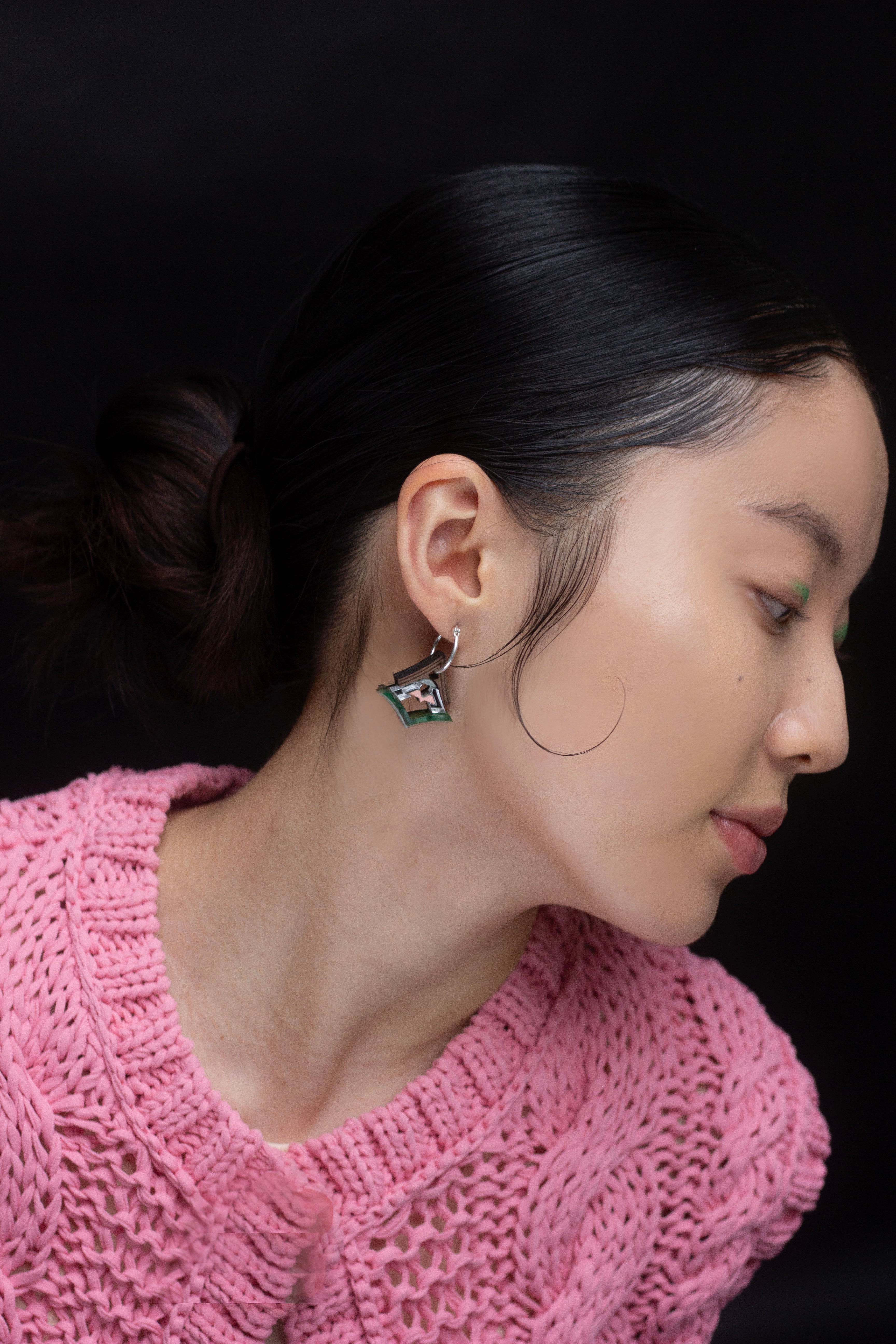 Woman wearing a pink knitted sweater and earrings against a black background