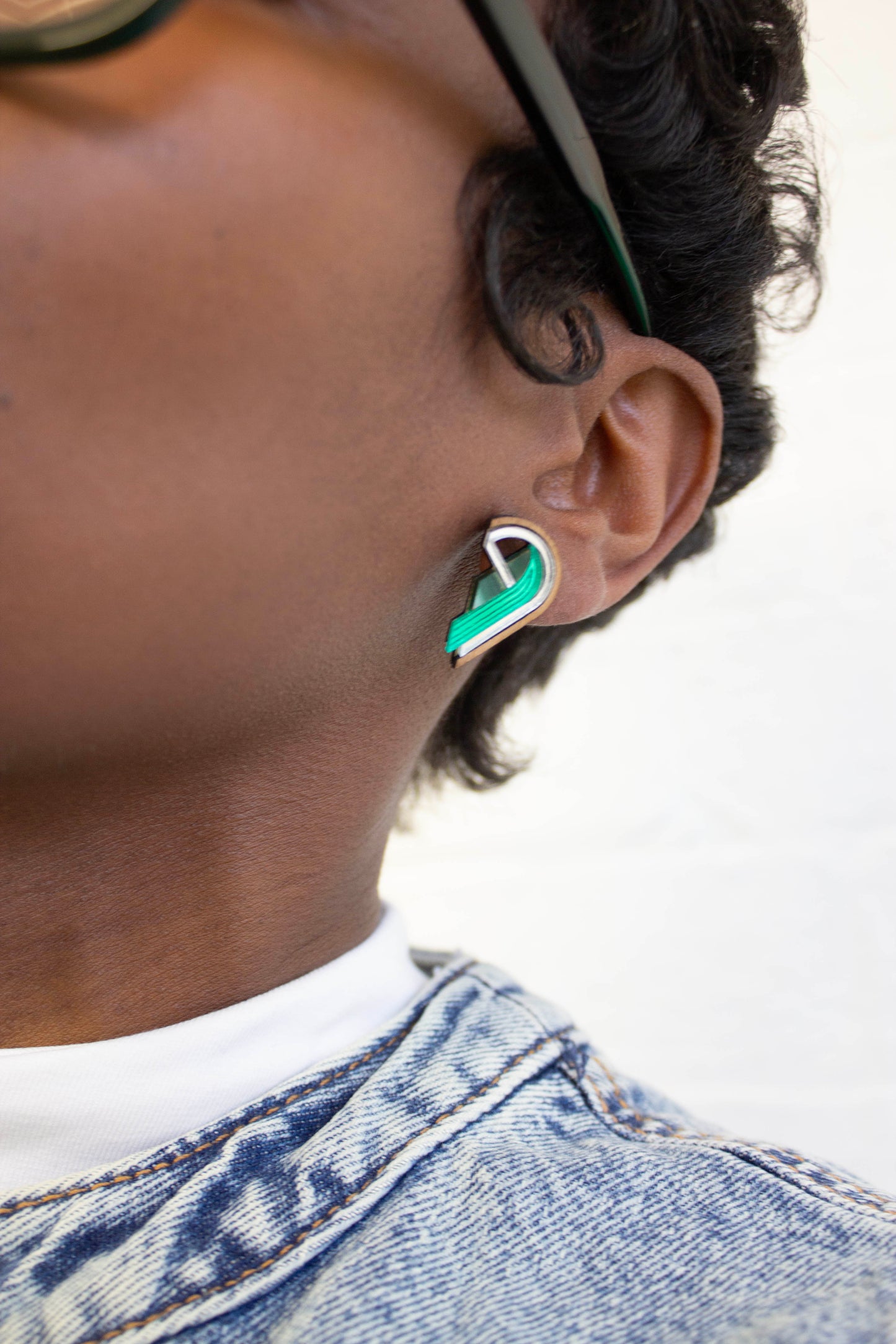 Person wearing a half heart shaped earring with a green and silver accents on a white background. made from acrylic, walnut wood and plywood