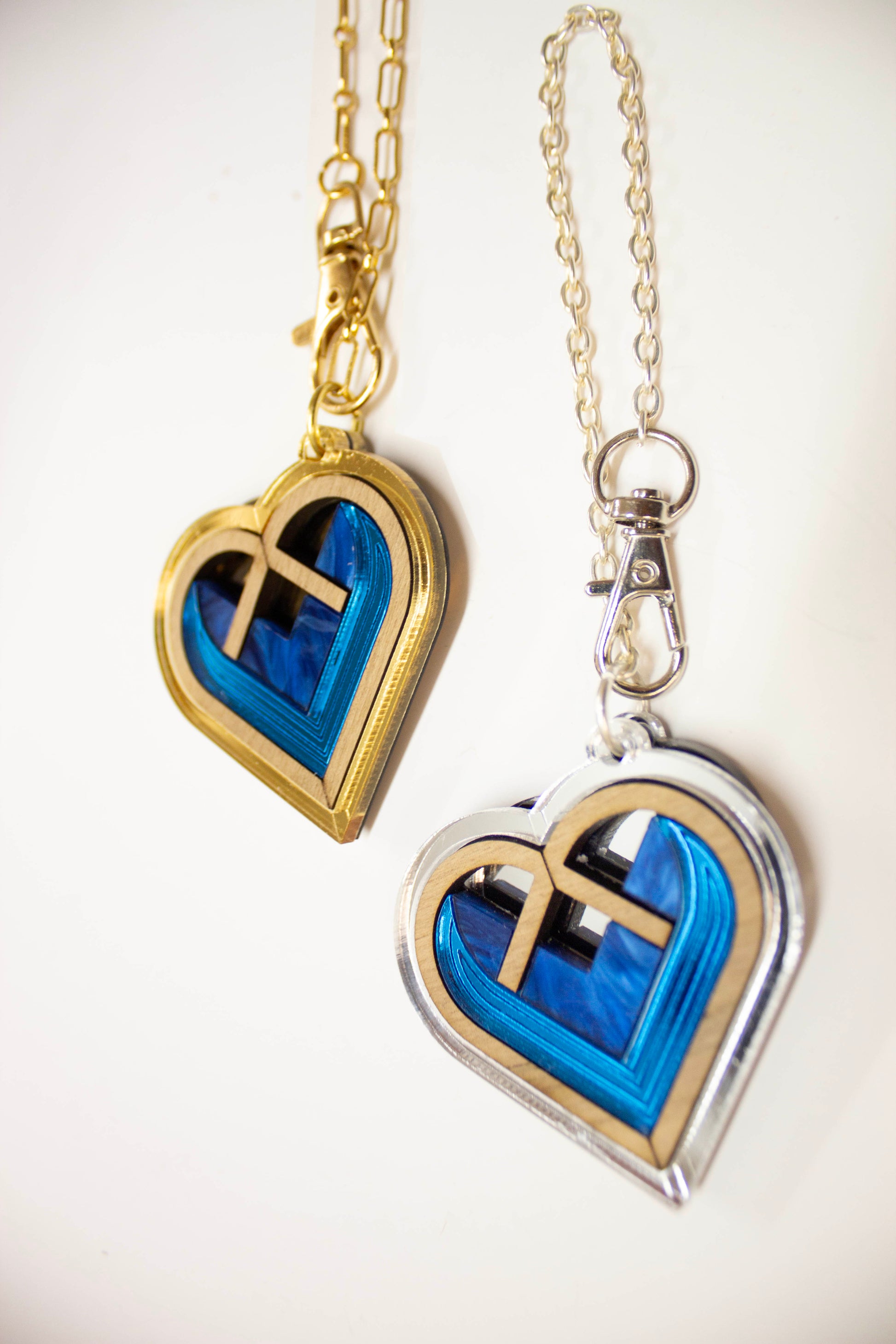 Heart-shaped bag charms with blue interior and gold/ silver border on a white background. Laser cut bag charms made from acrylic, walnut wood and plywood
