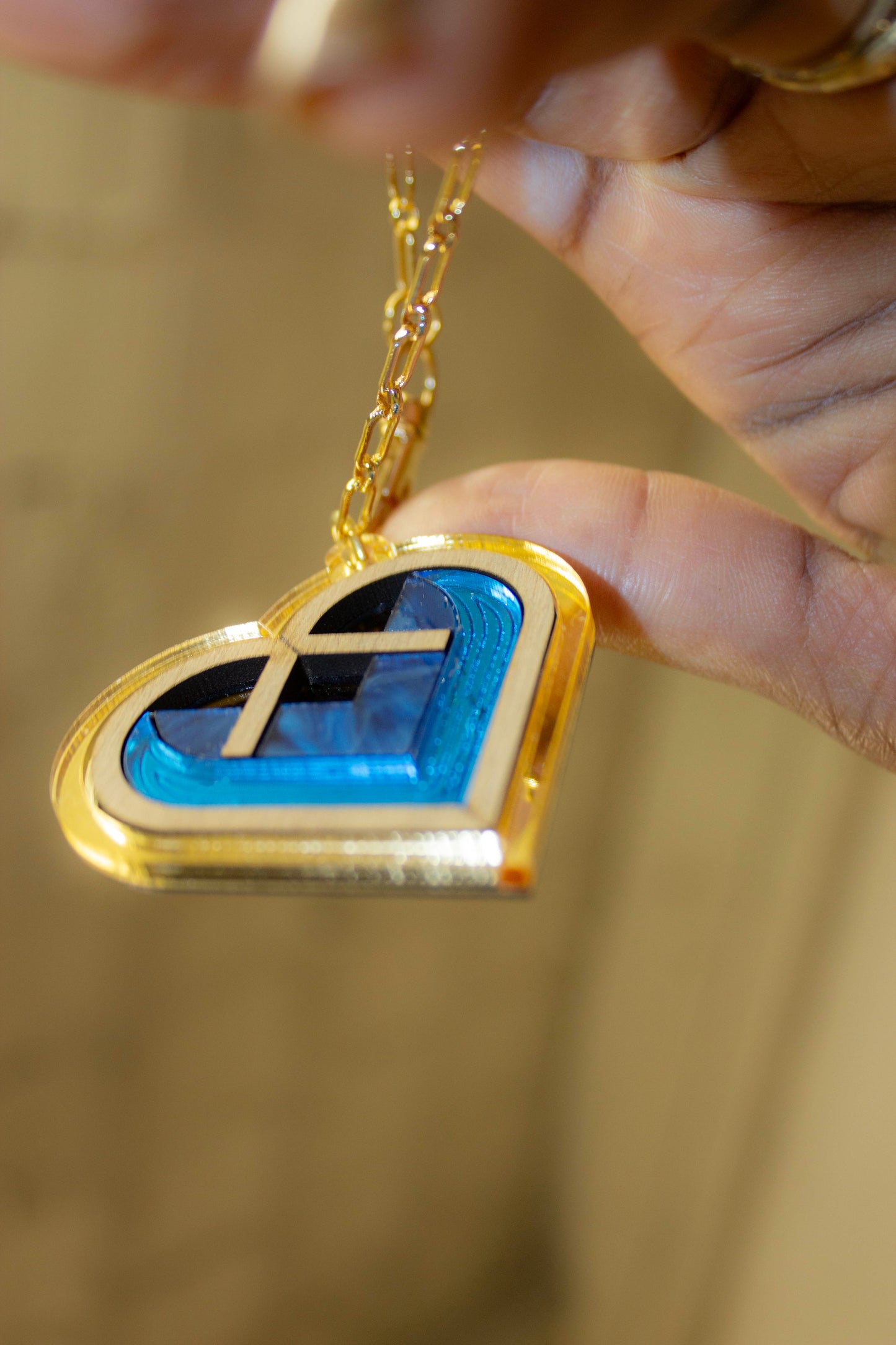 Heart-shaped pendant with blue center and gold frame held by a hand against a blurred background
