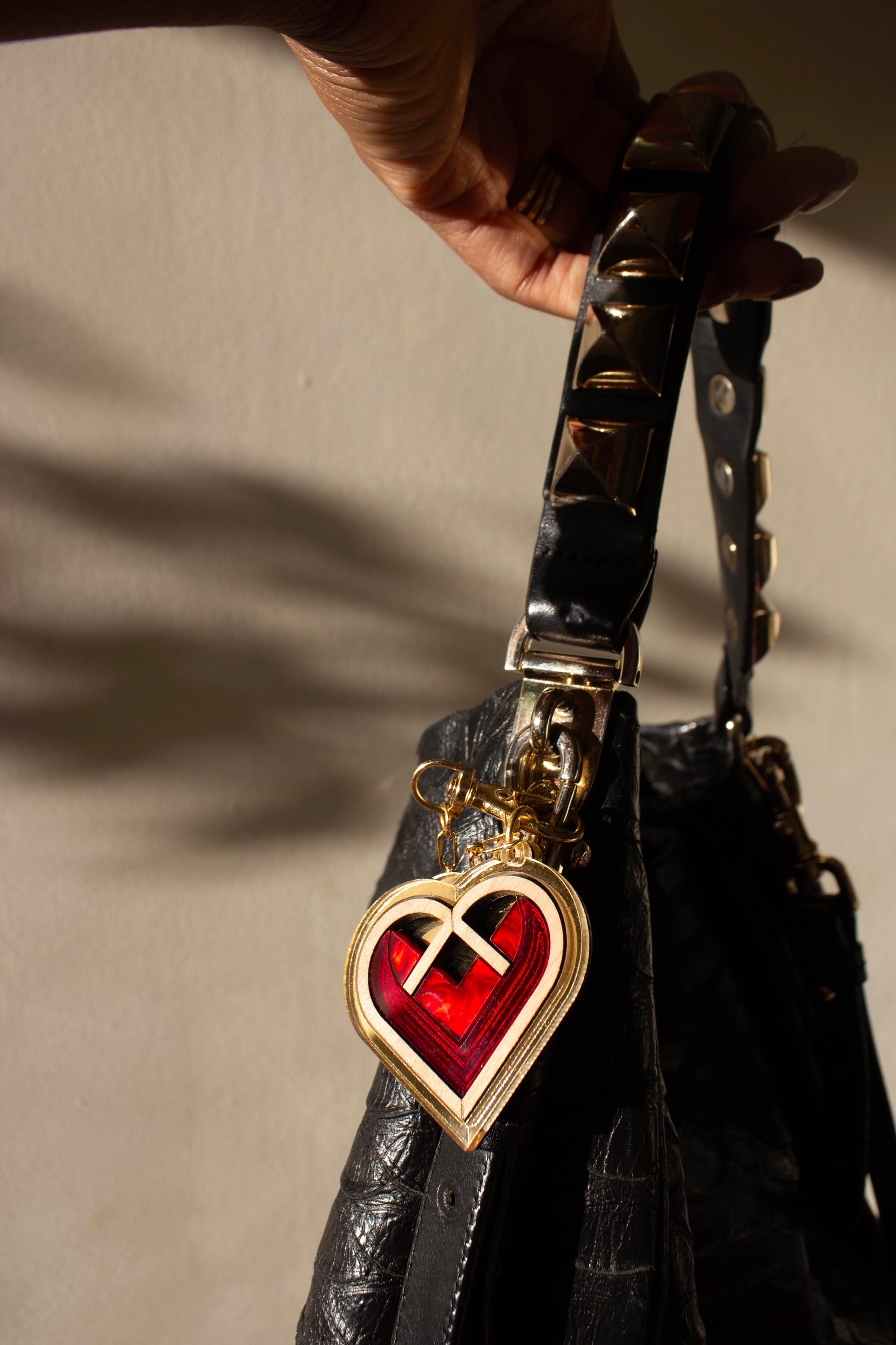 Black handbag with a gold and red heart-shaped bag charm on a neutral background. Laser cut charm made from plywood, walnut wood and acrylic