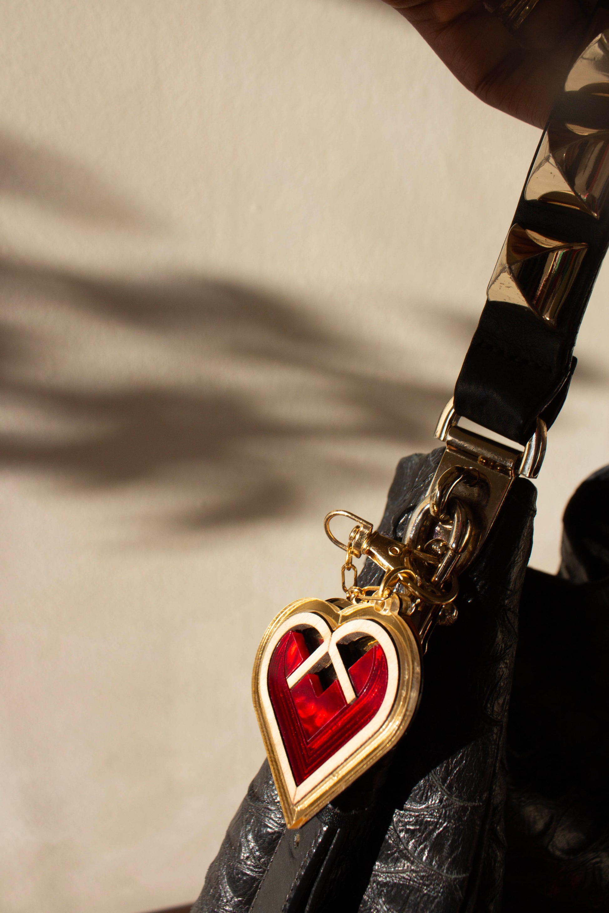 Heart-shaped bag charm with red center and gold border on a beige background. Laser cut charm made from acrylic, plywood and walnut wood. 
