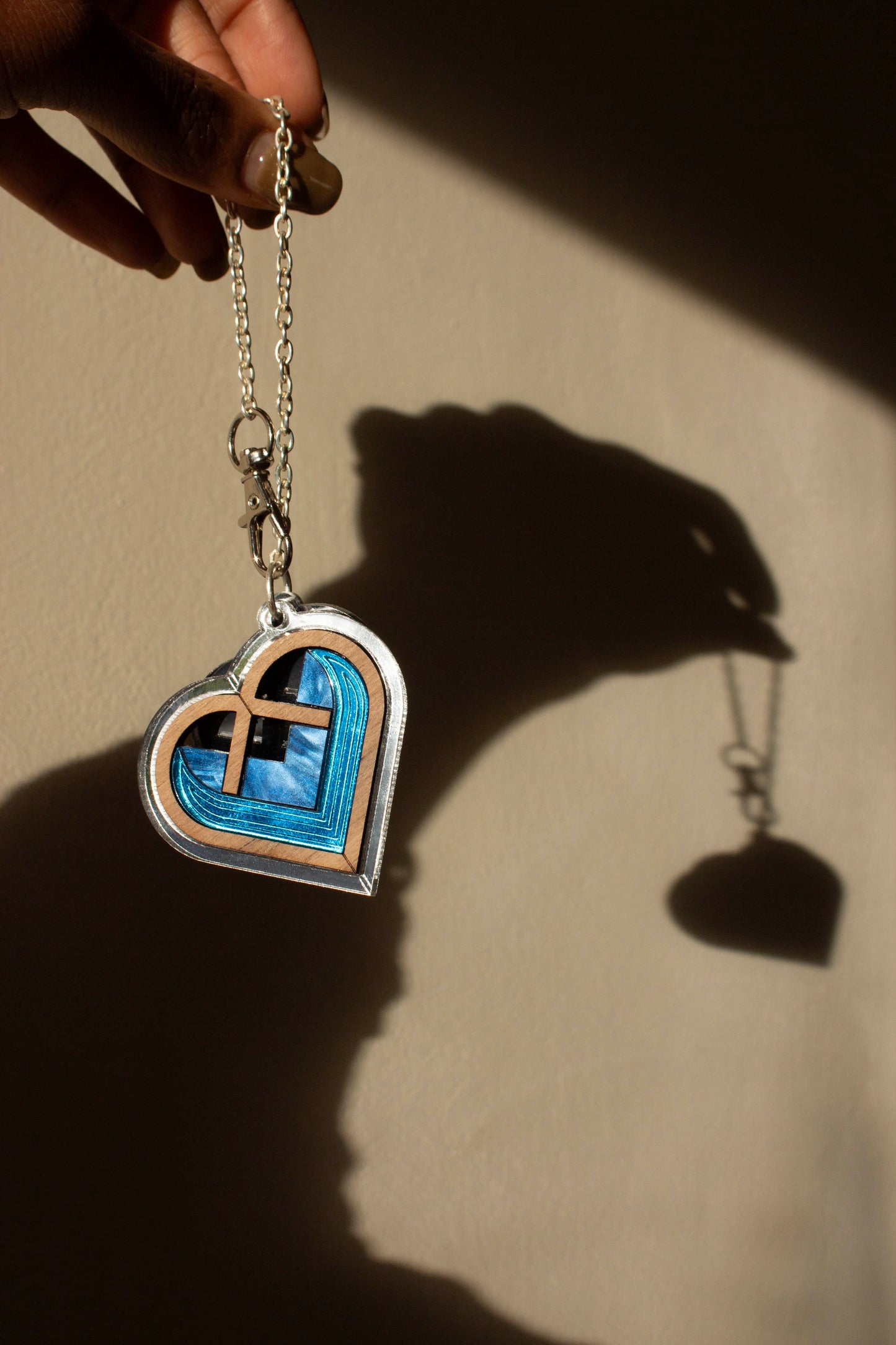 Heart-shaped pendant with blue interior and silver accents on a silver plated chain, held against a beige background.