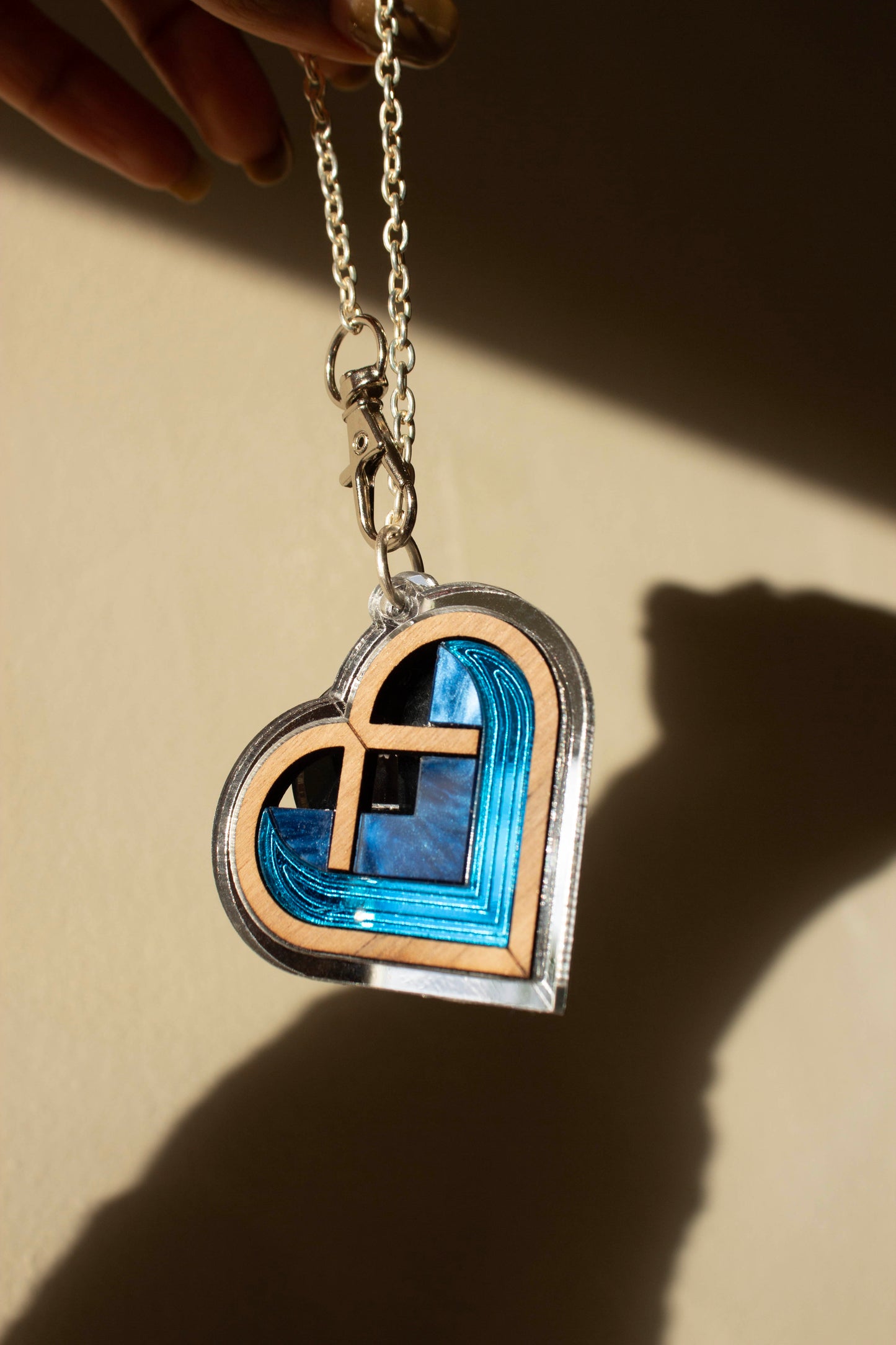 Heart-shaped acrylic bag charm with a silver border and blue interior on a beige background