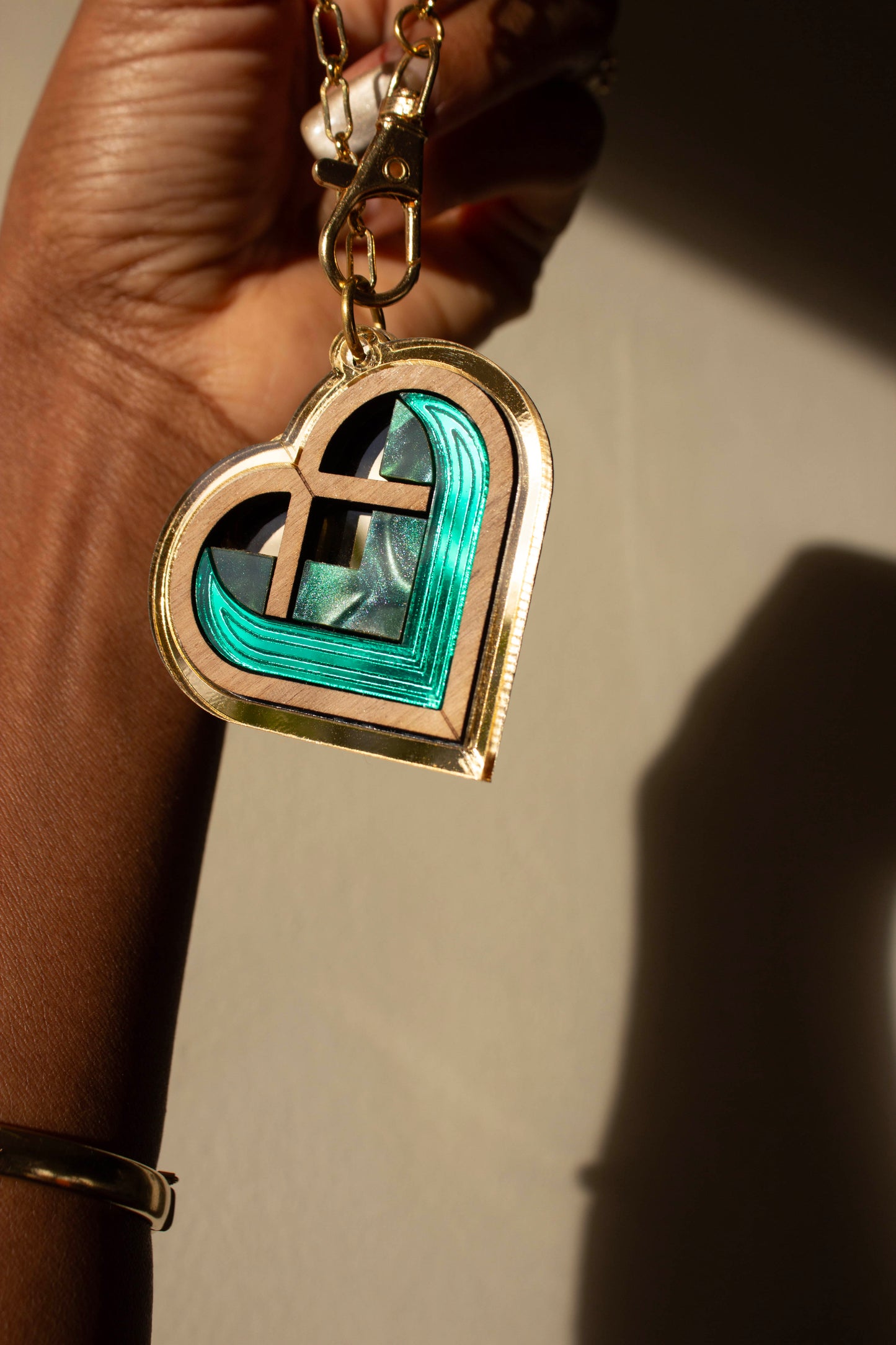 Heart-shaped gold bag charm with green interior held by a hand against a neutral background. Laser cut charm made from acrylic, walnut wood and plywood 