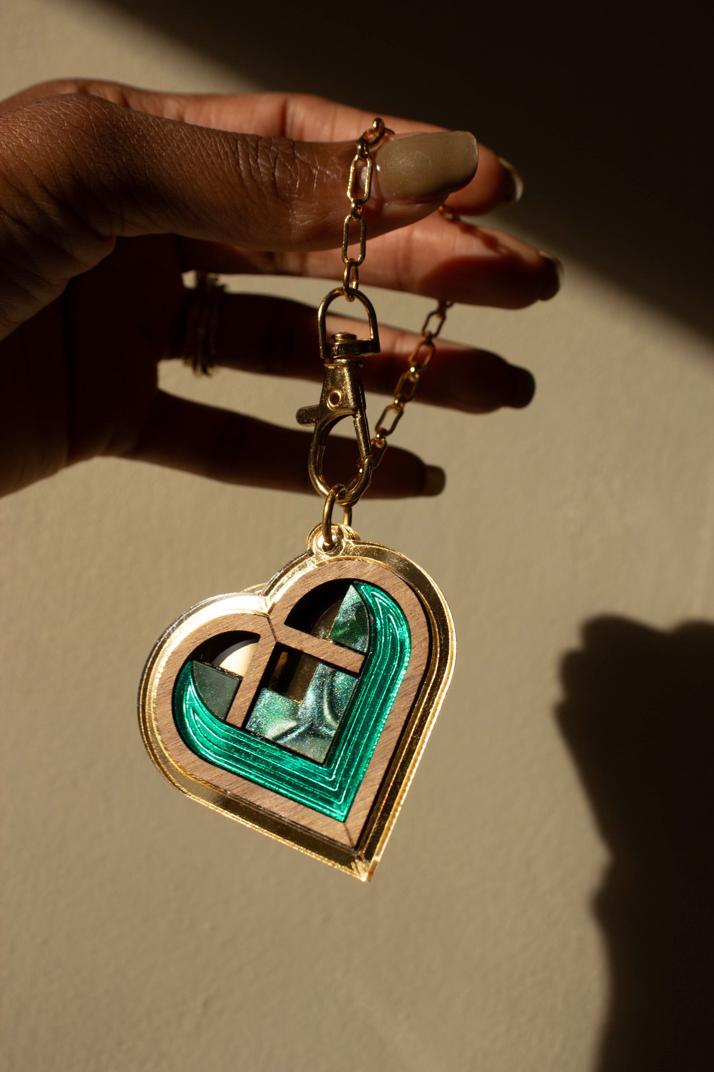 Gold heart-shaped bag charm with gold border and green interior held by a hand against a neutral background