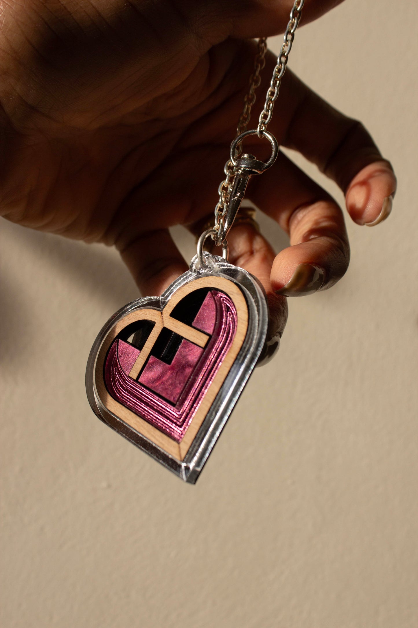 Heart-shaped acrylic bag charm with a silver border and pink interior held by a hand against a beige background