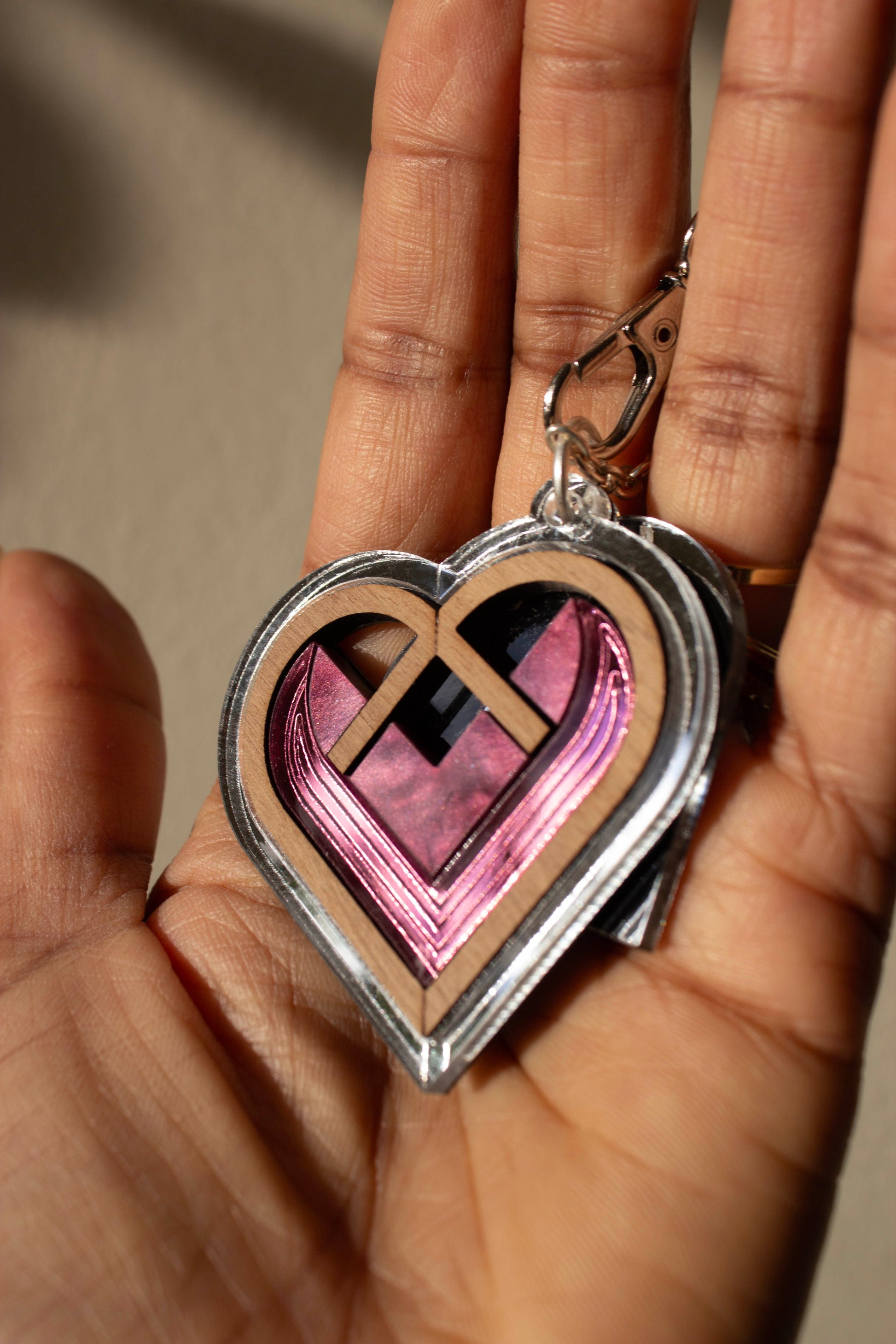Heart-shaped bag charm with silver border and pink interior held in a hand against a neutral background