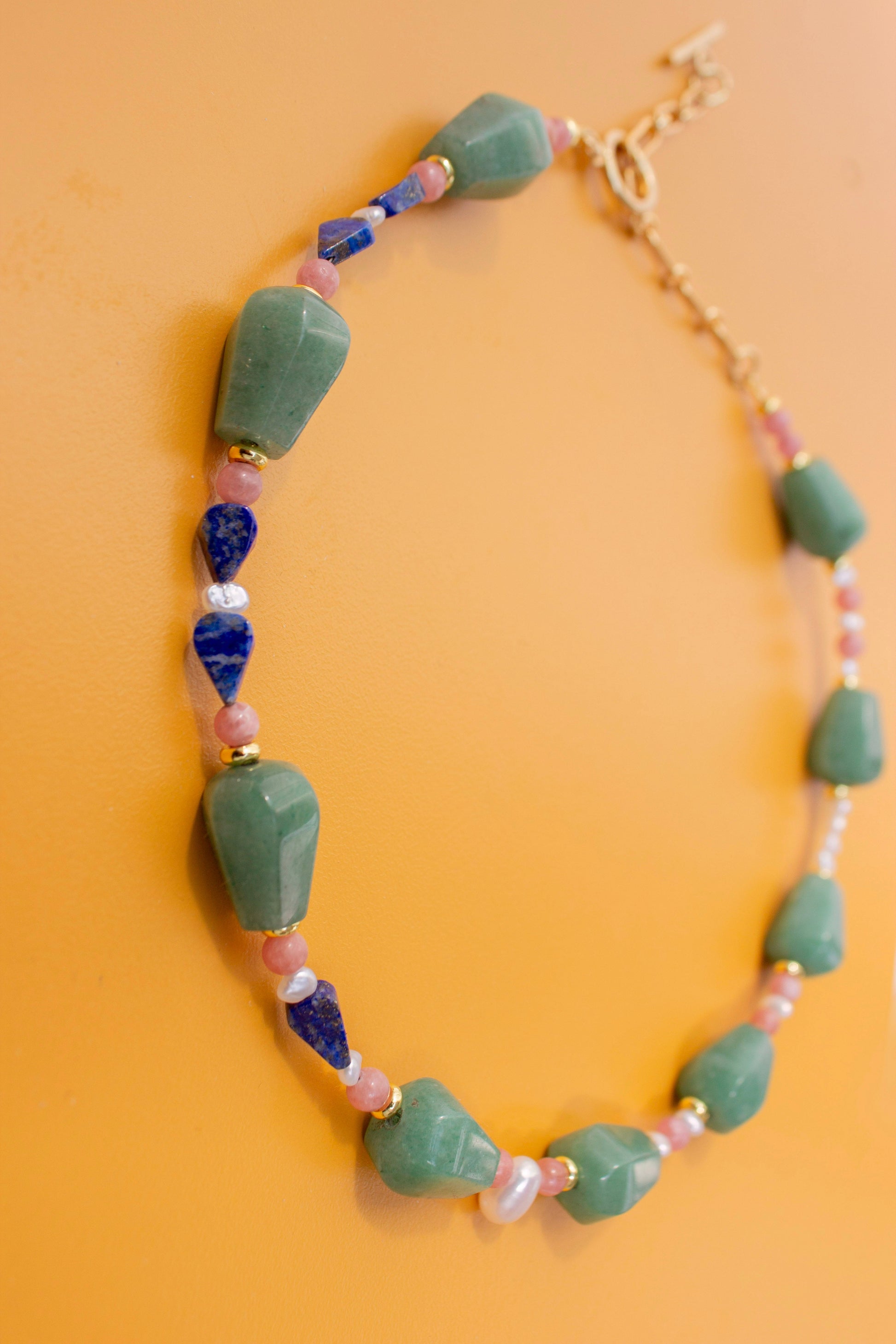 Necklace with green aventurine, lapis, pearl and rhodochrosite beads and gold chain on an orange background