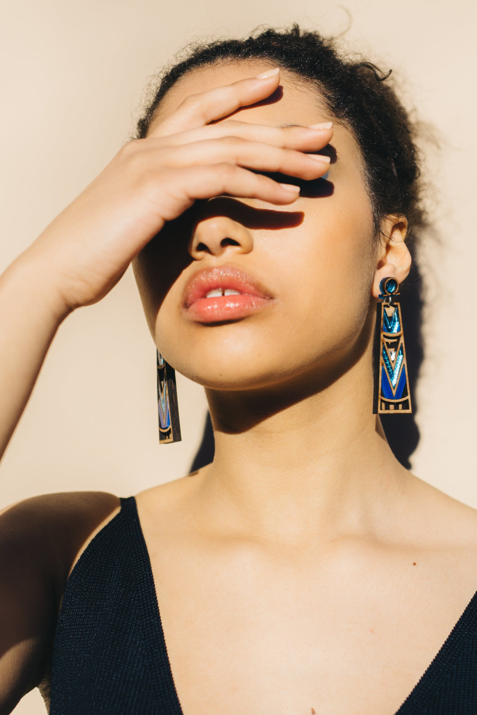 Woman wearing large, colourful geometric earrings with a neutral background