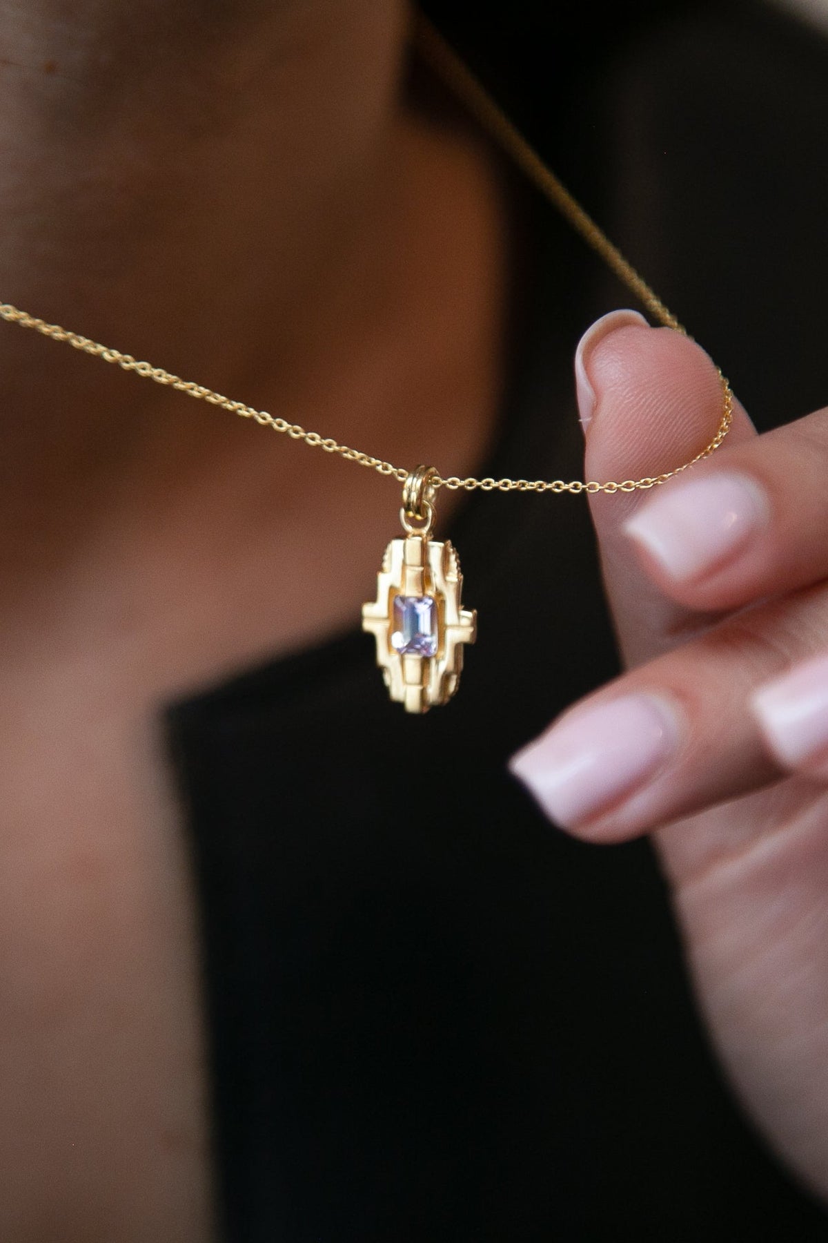 close up of a woman holding a gold geometric necklace with an ametrine gemstone