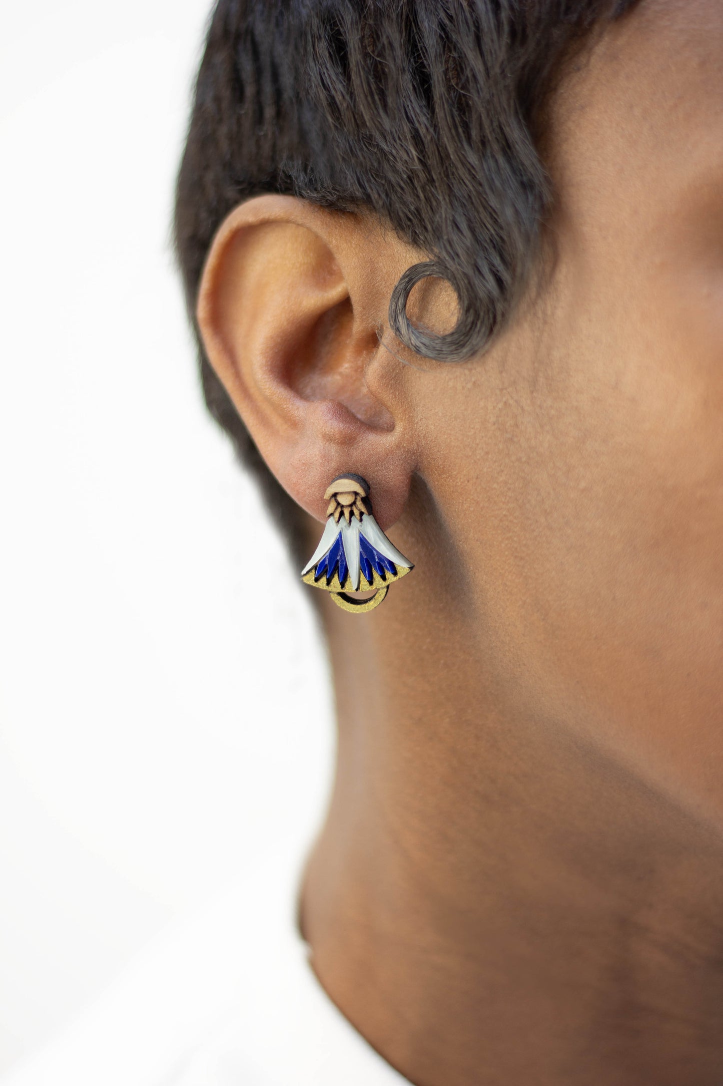 Close-up of an ear wearing a blue and gold lotus earring with a white background