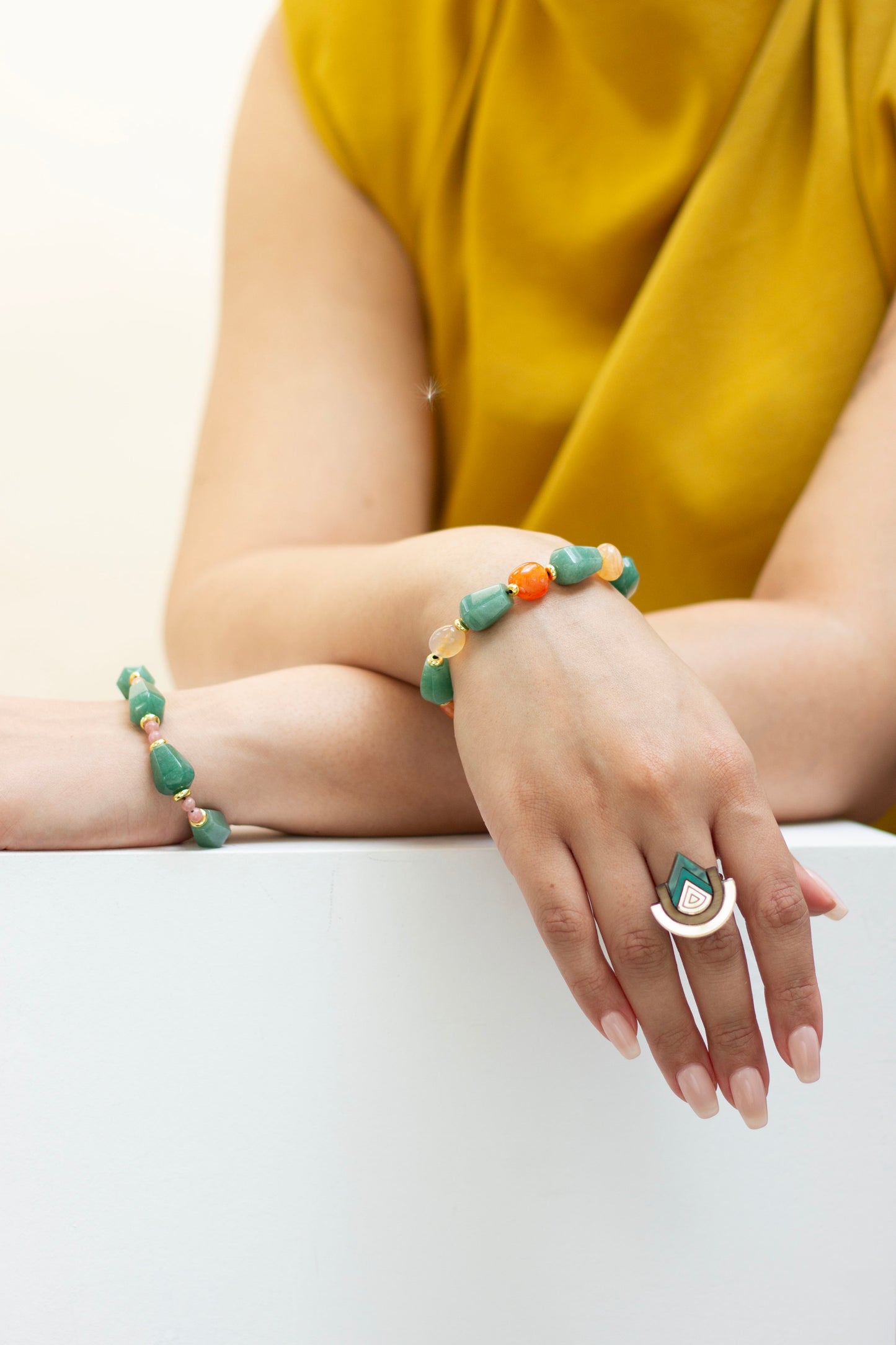 Person wearing a green aventurine and carnelian beaded bracelet and ring on a white surface