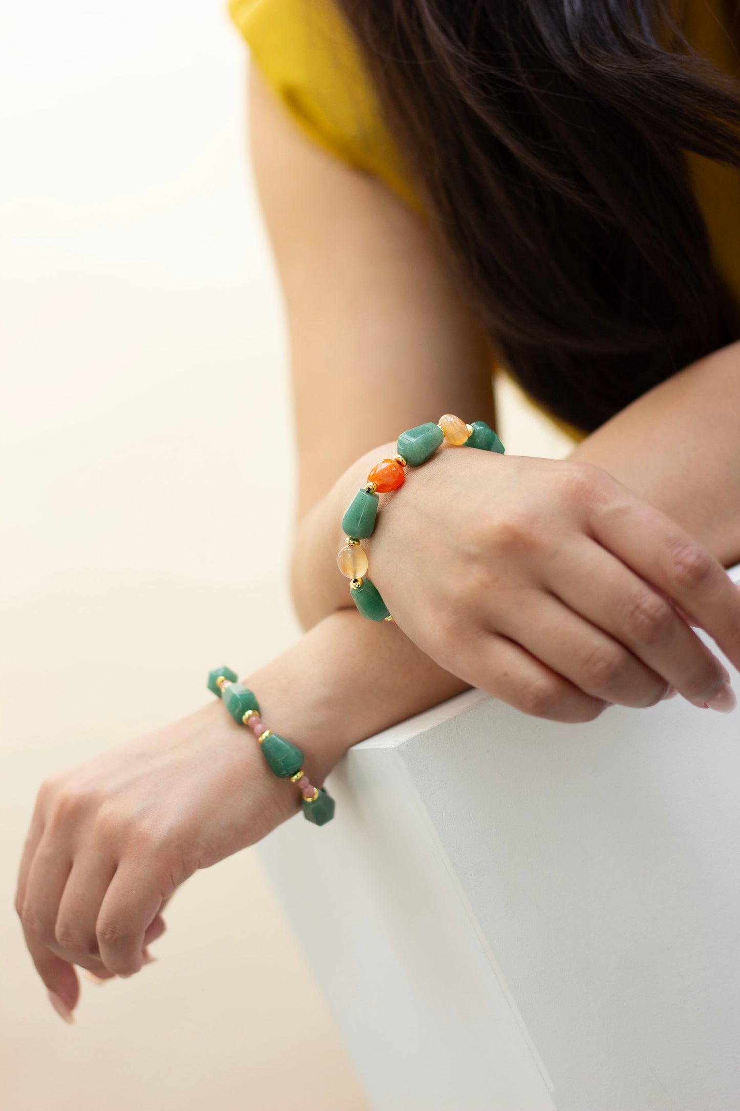 Close-up of a person wearing a aventurine and carnelian colourful beaded bracelets on a plain background