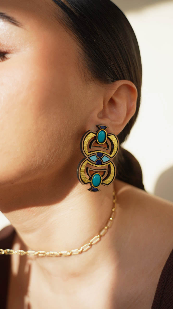 Close-up of a person wearing a decorative scarab earring with turquoise stones and gold accents.