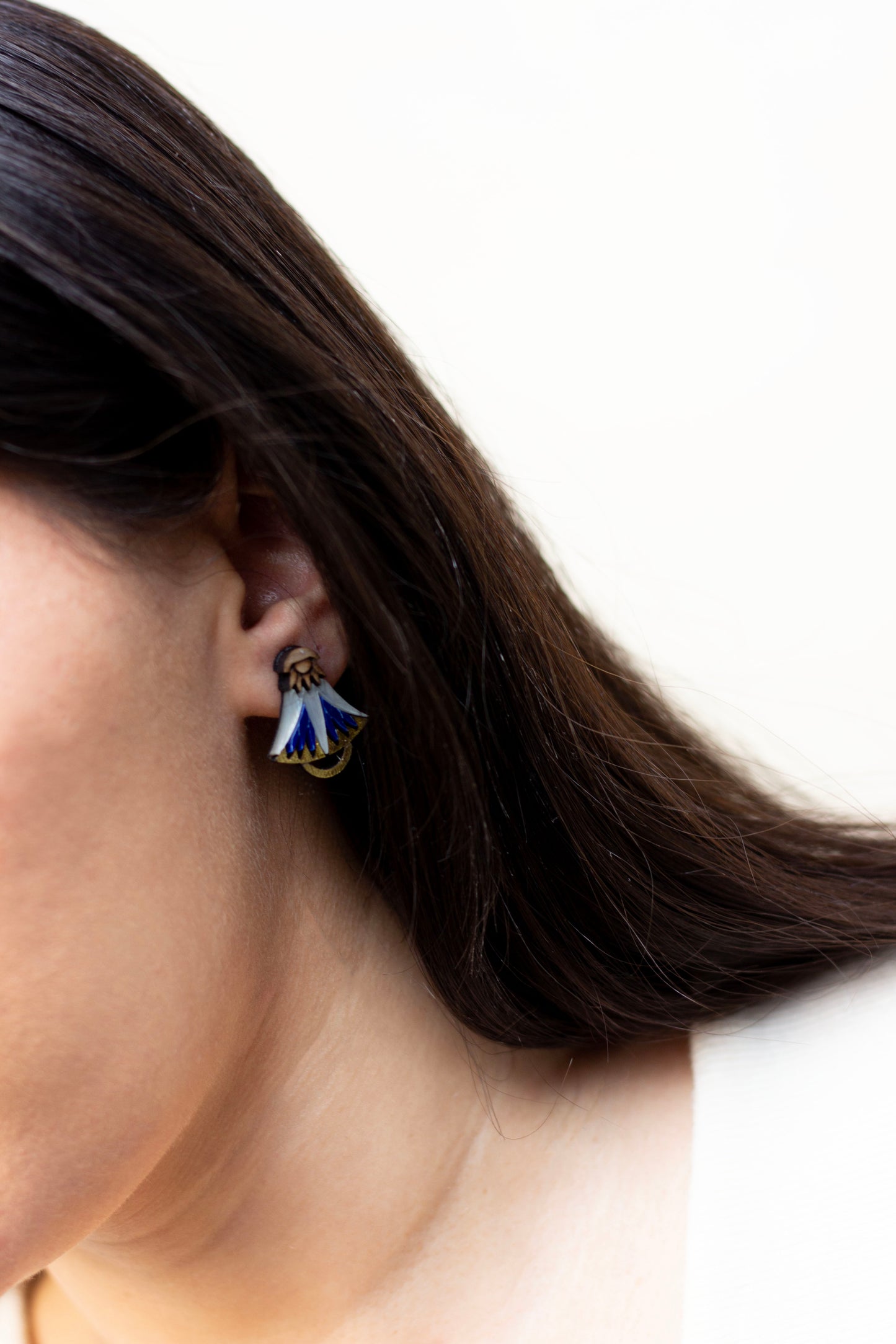 Close-up of a person wearing a blue and gold lotus earring with a plain background