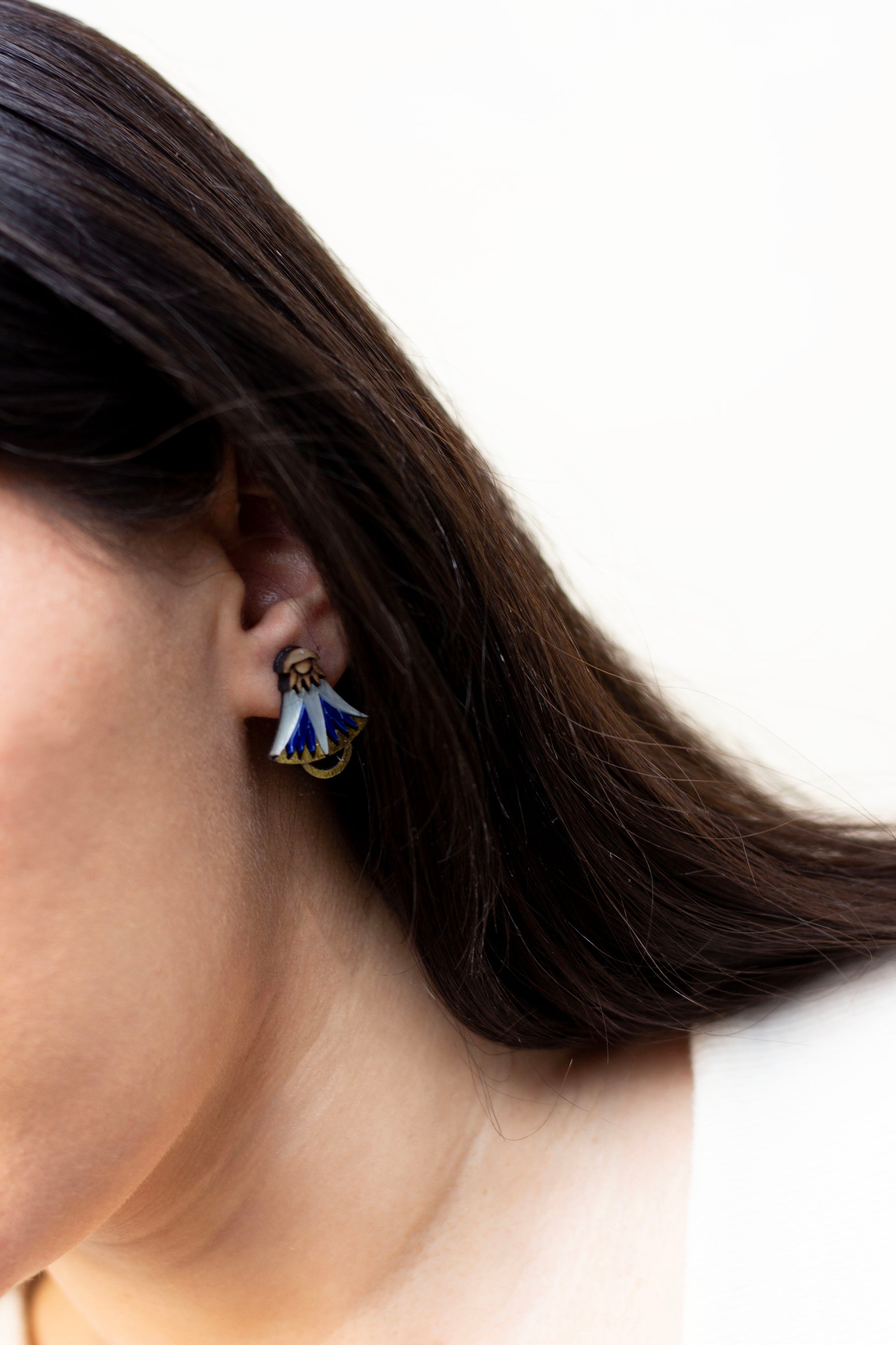 Close-up of a person wearing a blue and gold lotus earring with a plain background