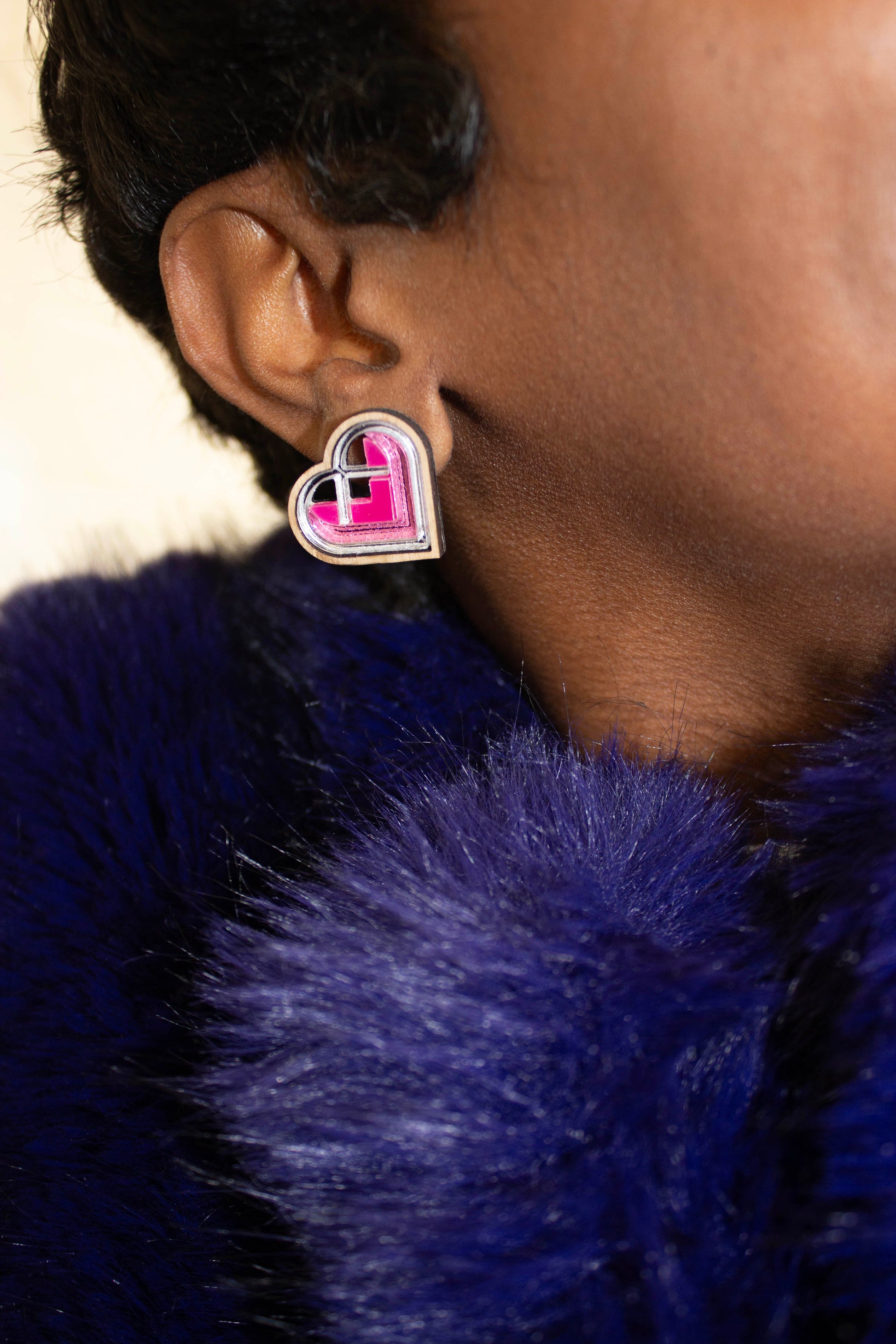 Pink and silver Heart-shaped earrings worn by a person with a blue fur coat. Laser cut earring made from walnut and acrylic