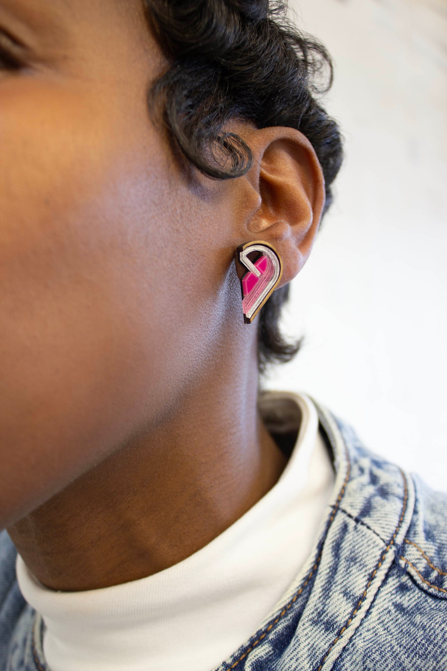 Person wearing a pink and silver half heart-shaped earring made from acrylic, plywood and walnut wood 