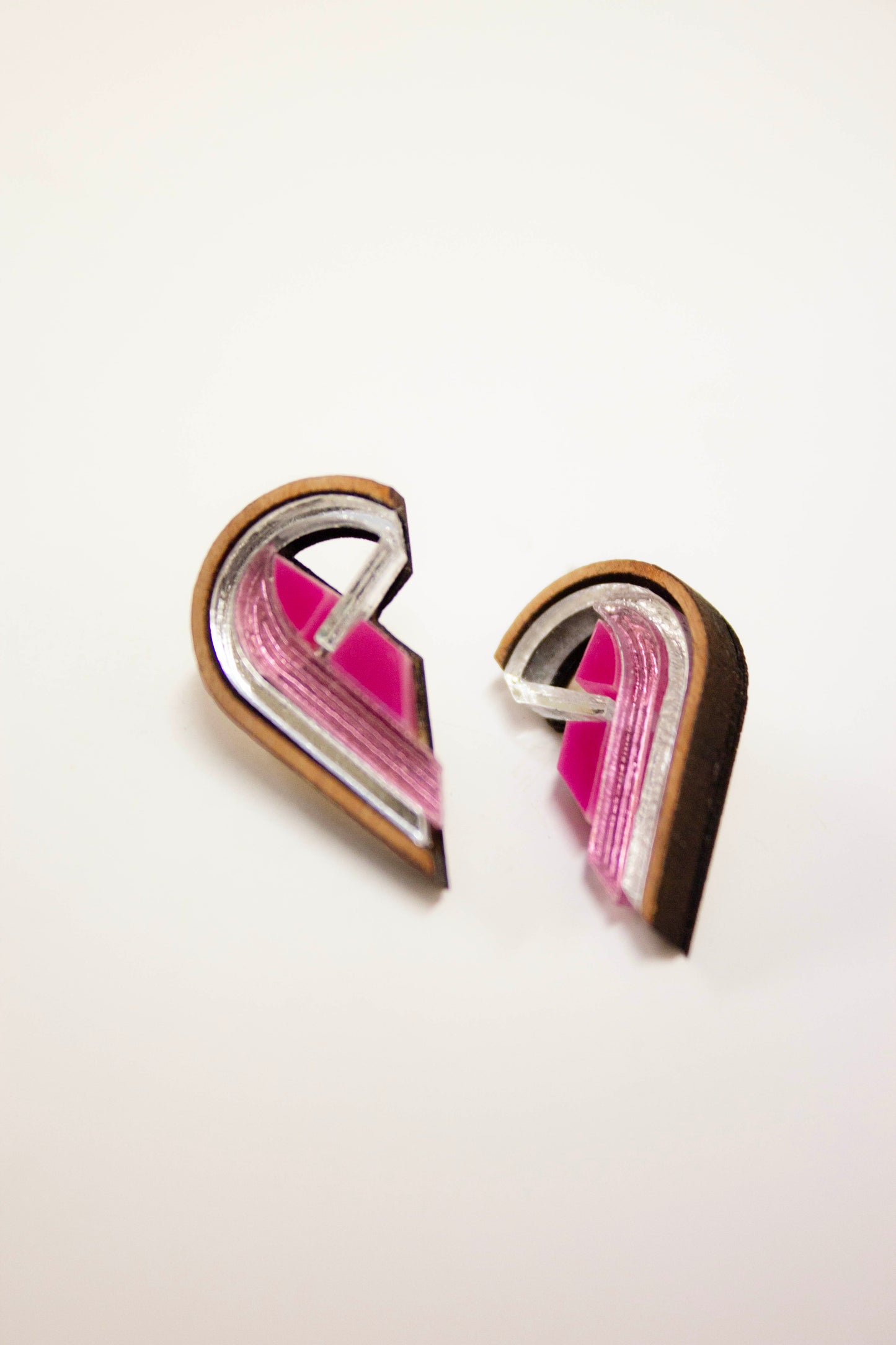 Semi Heart-shaped earrings with pink and silver design on a white background. Laser cut earrings made from acrylic, walnut wood and plywood