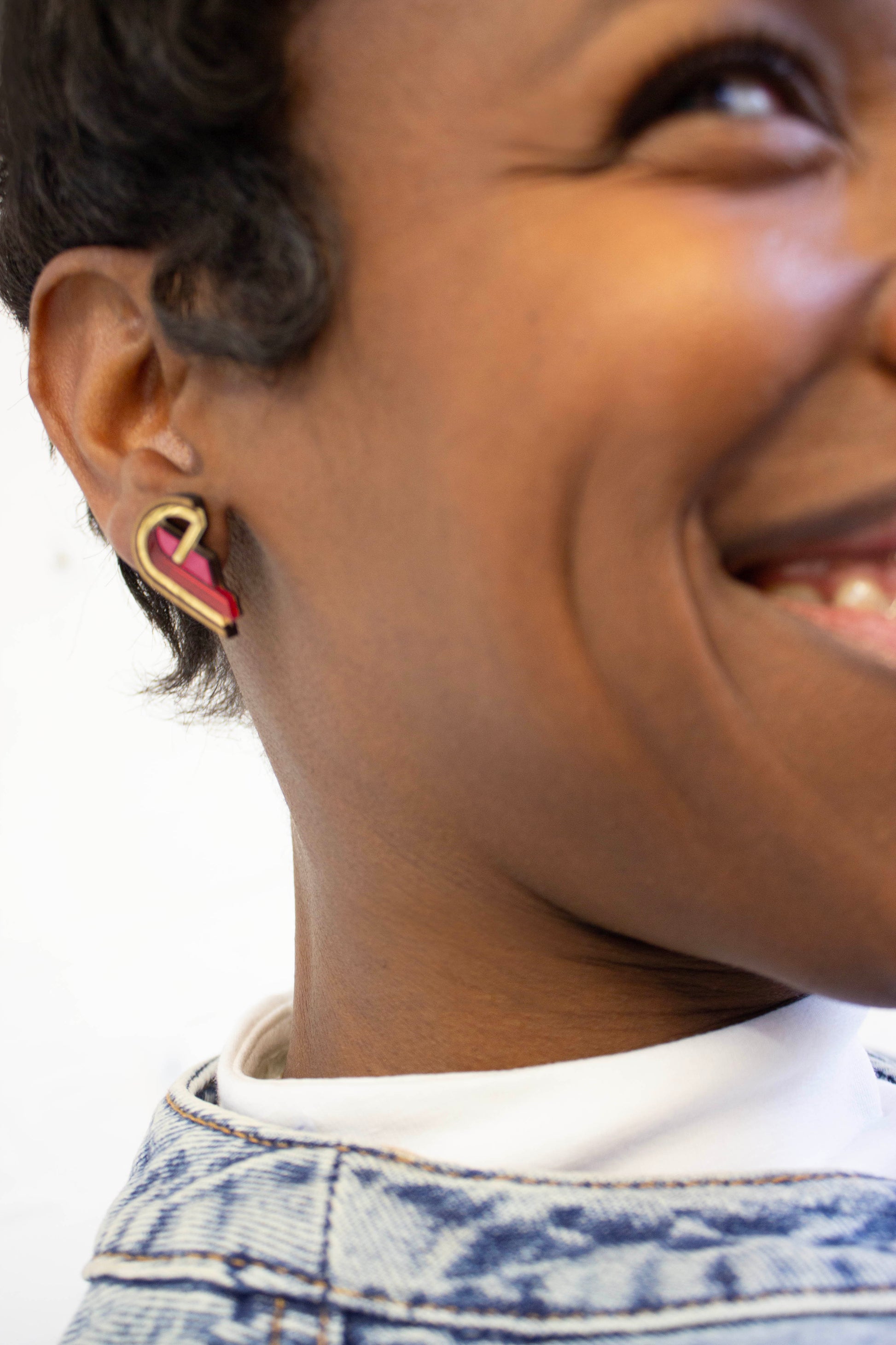 Close-up of a person wearing a gold and red heart-shaped acrylic earring with a walnut wood border