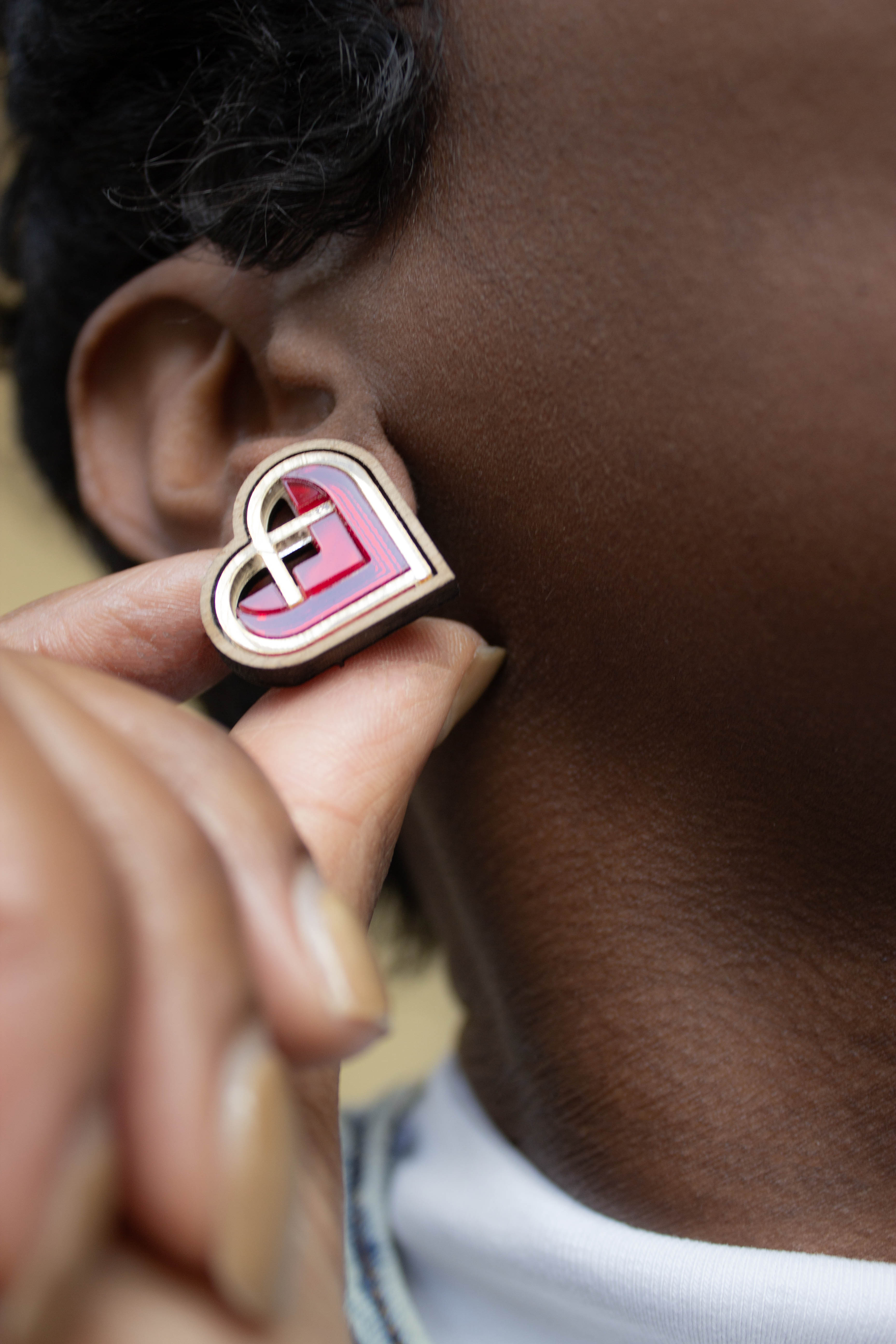 Heart-shaped red and gold earring being worn on an ear. laser cut earring, made from walnut wood and acrylic