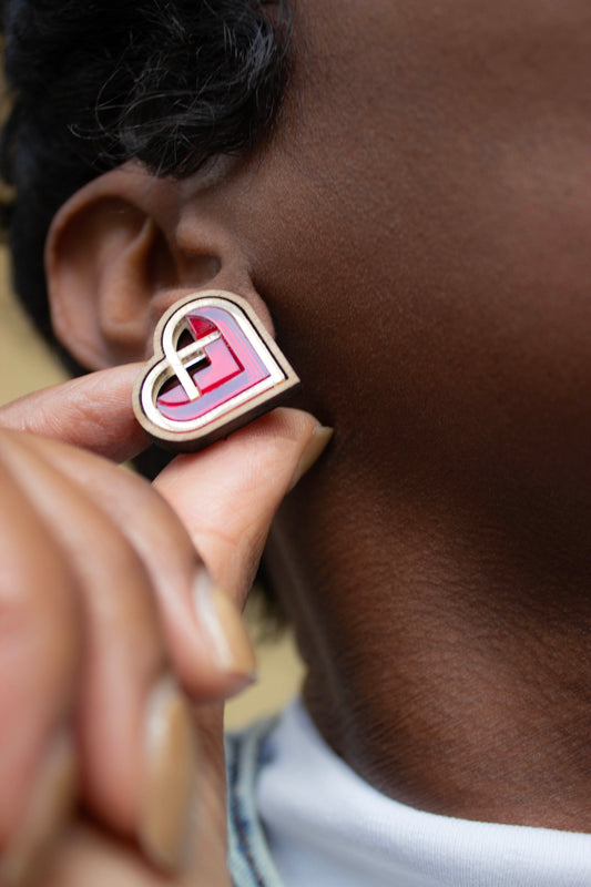 Heart-shaped red and gold earring being worn on an ear. laser cut earring, made from walnut wood and acrylic