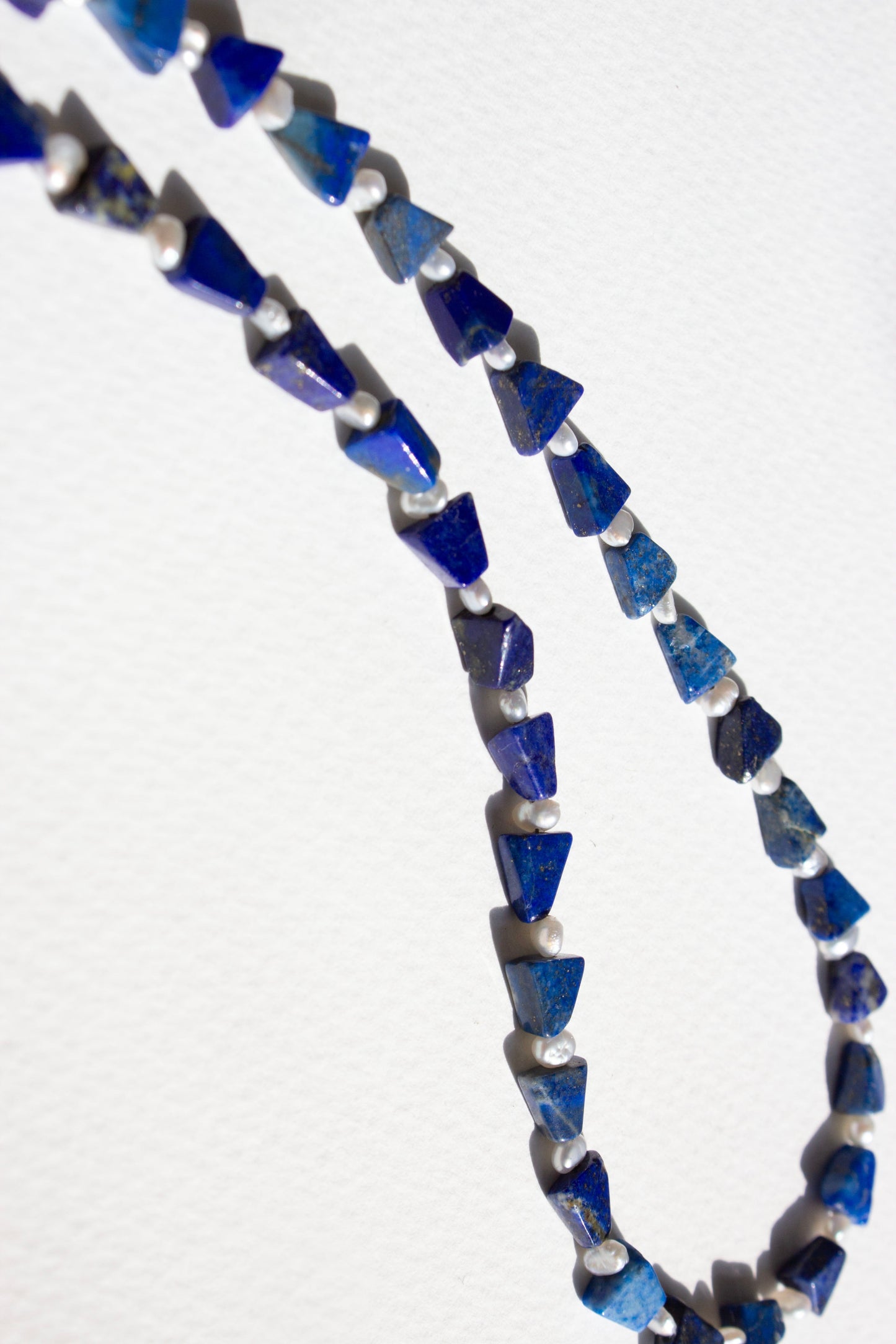 Necklace with blue lapis and pearl beads on a white background