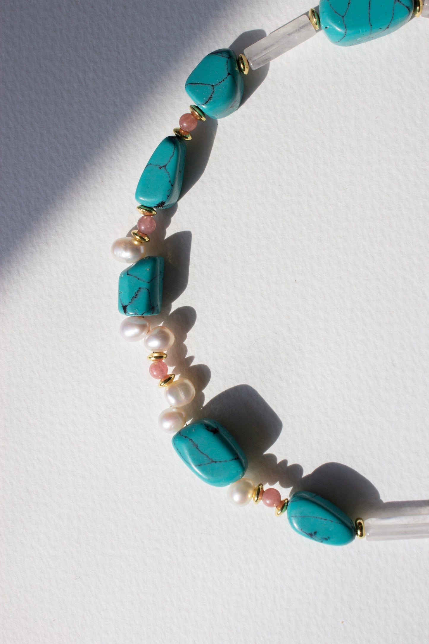 Necklace with turquoise, rose quartz and pearl beads on a white background