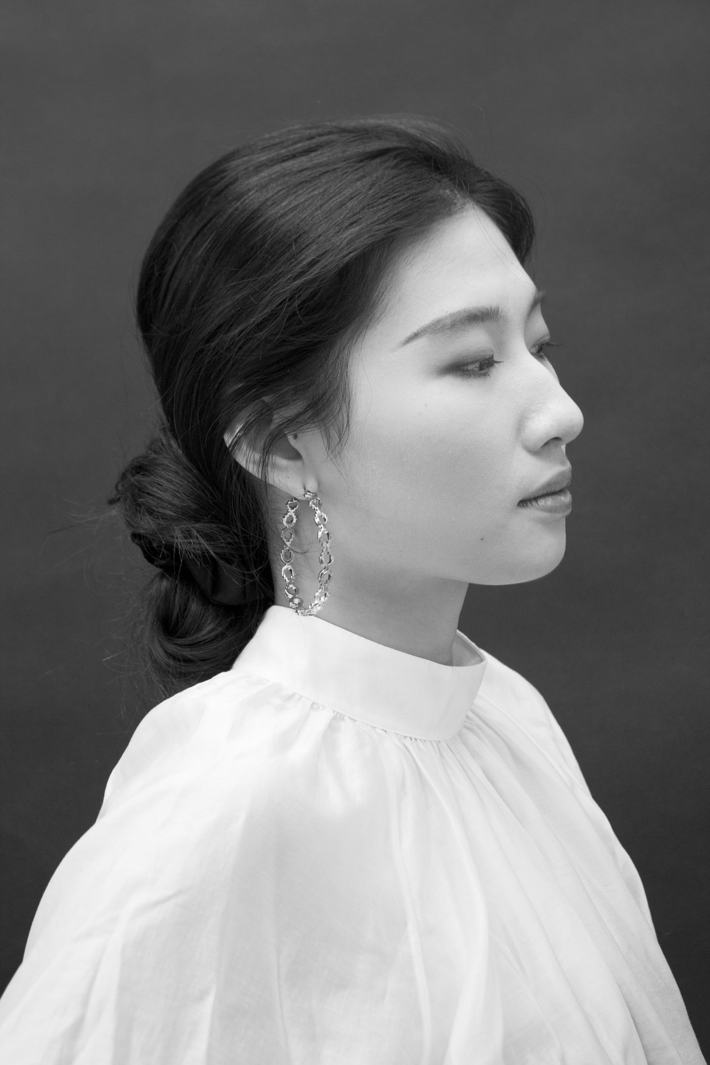 A black and white image of a woman wearing large silver hoop earrings.