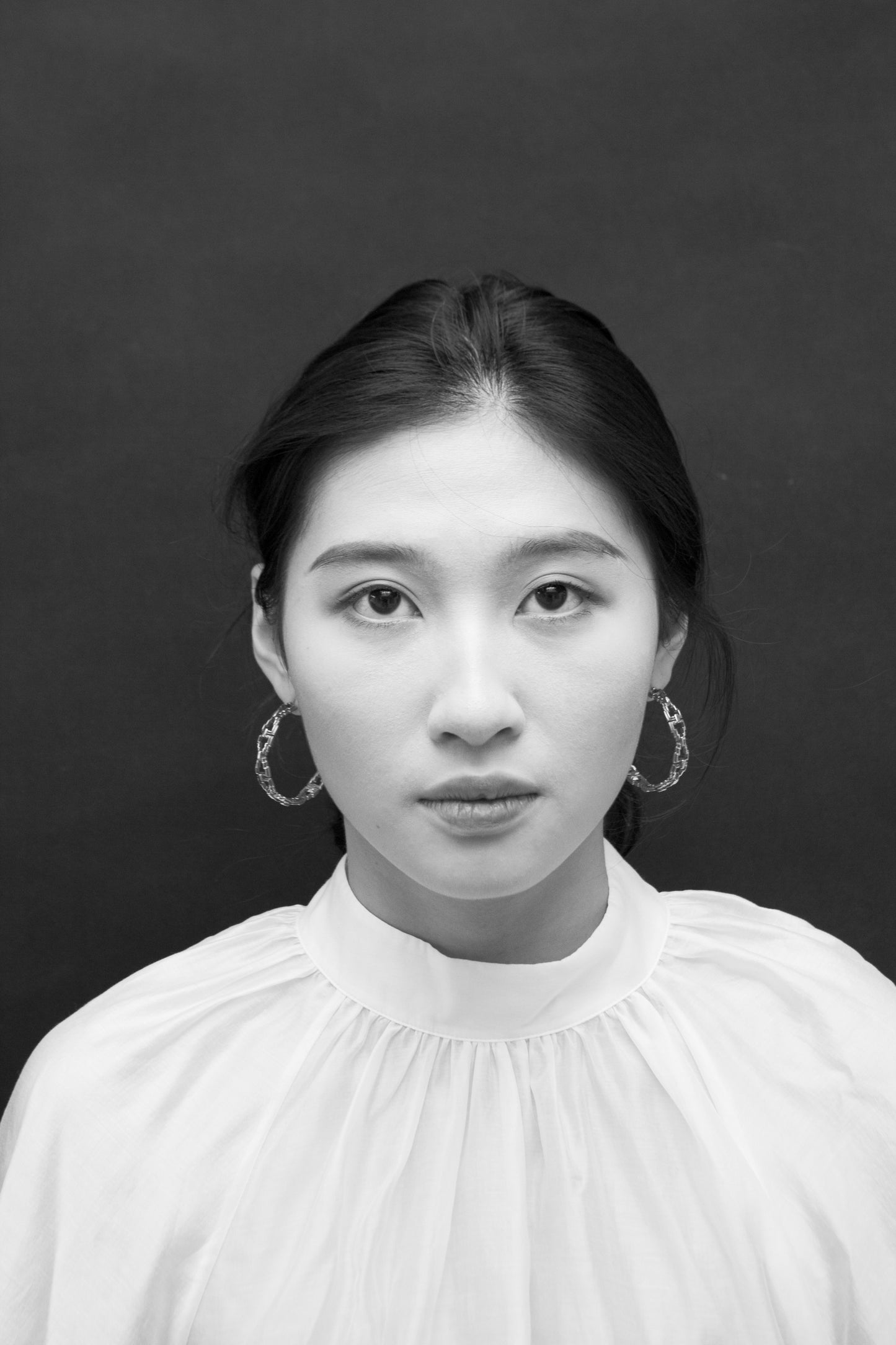 A person wearing a silver pair of hoop earrings with a dark background